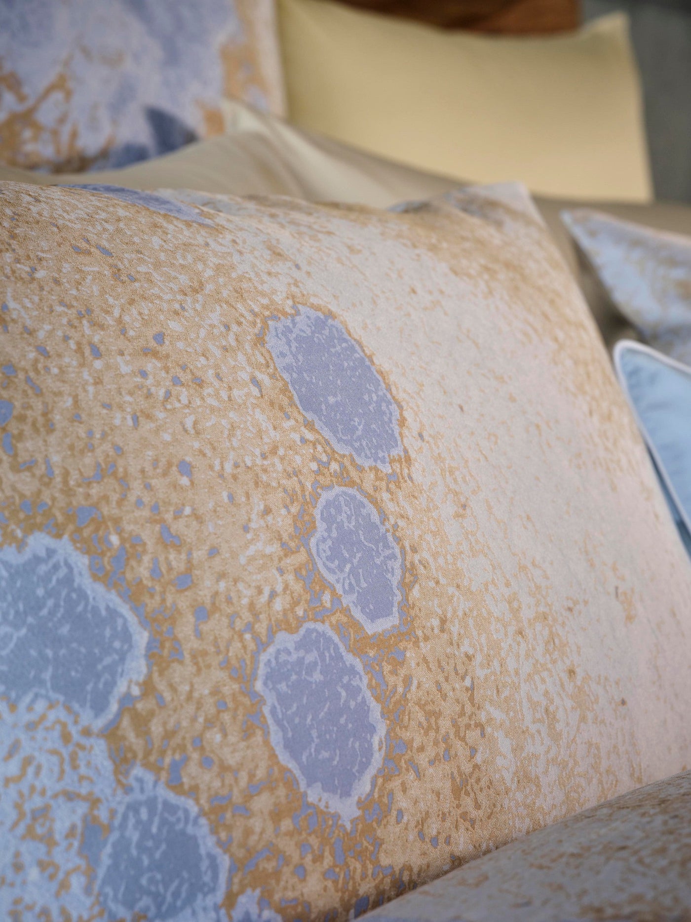Close-up on textured fabric with abstract patterns in tan and light blue, featuring Callisto Pillowcase by Celso de Lemos available at Linen Society.
