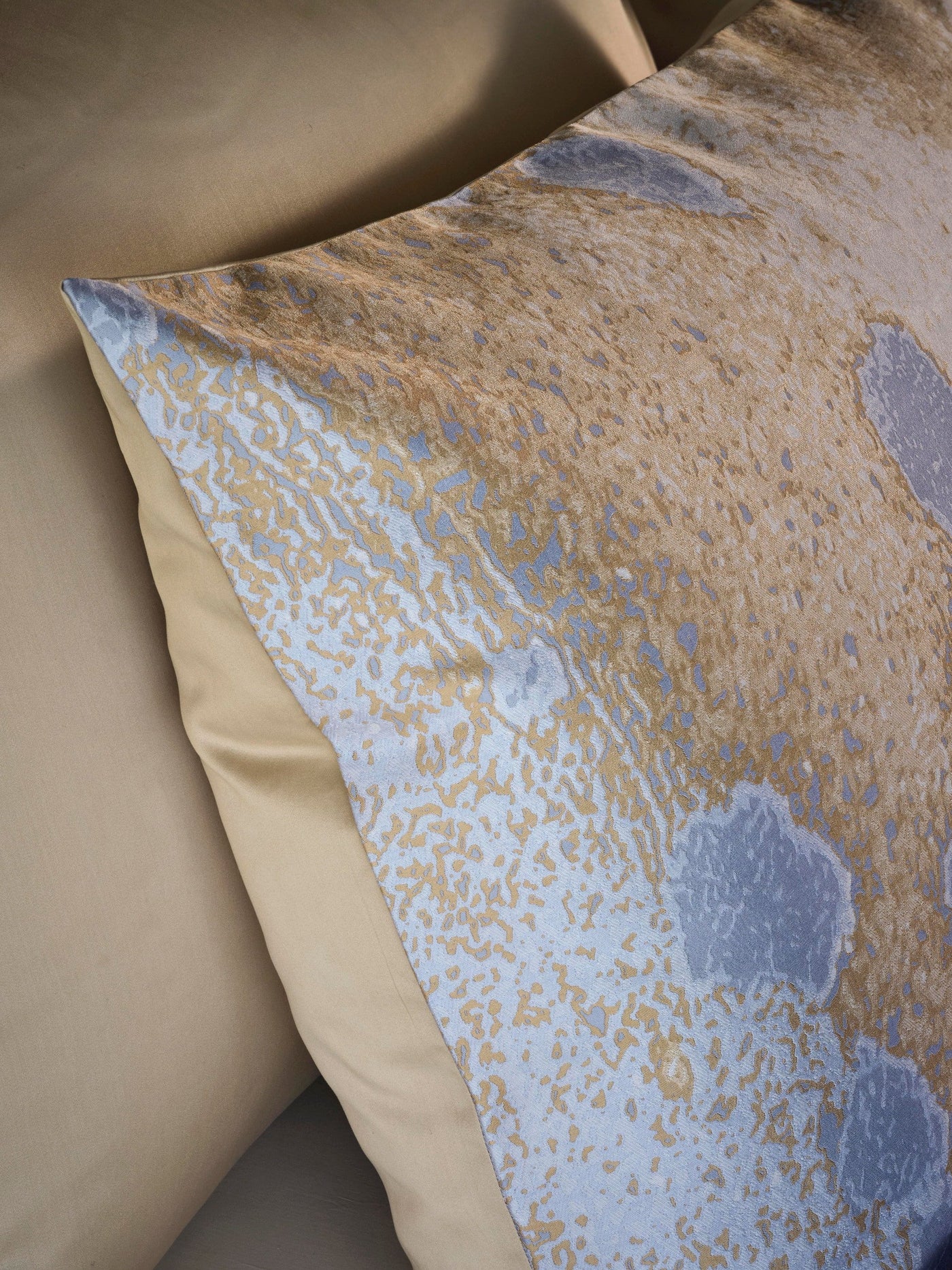 A close-up shot of a pillow with a textured, abstract pattern in gold and light blue, featuring the Callisto Pillowcase by Celso de Lemos available at Linen Society.