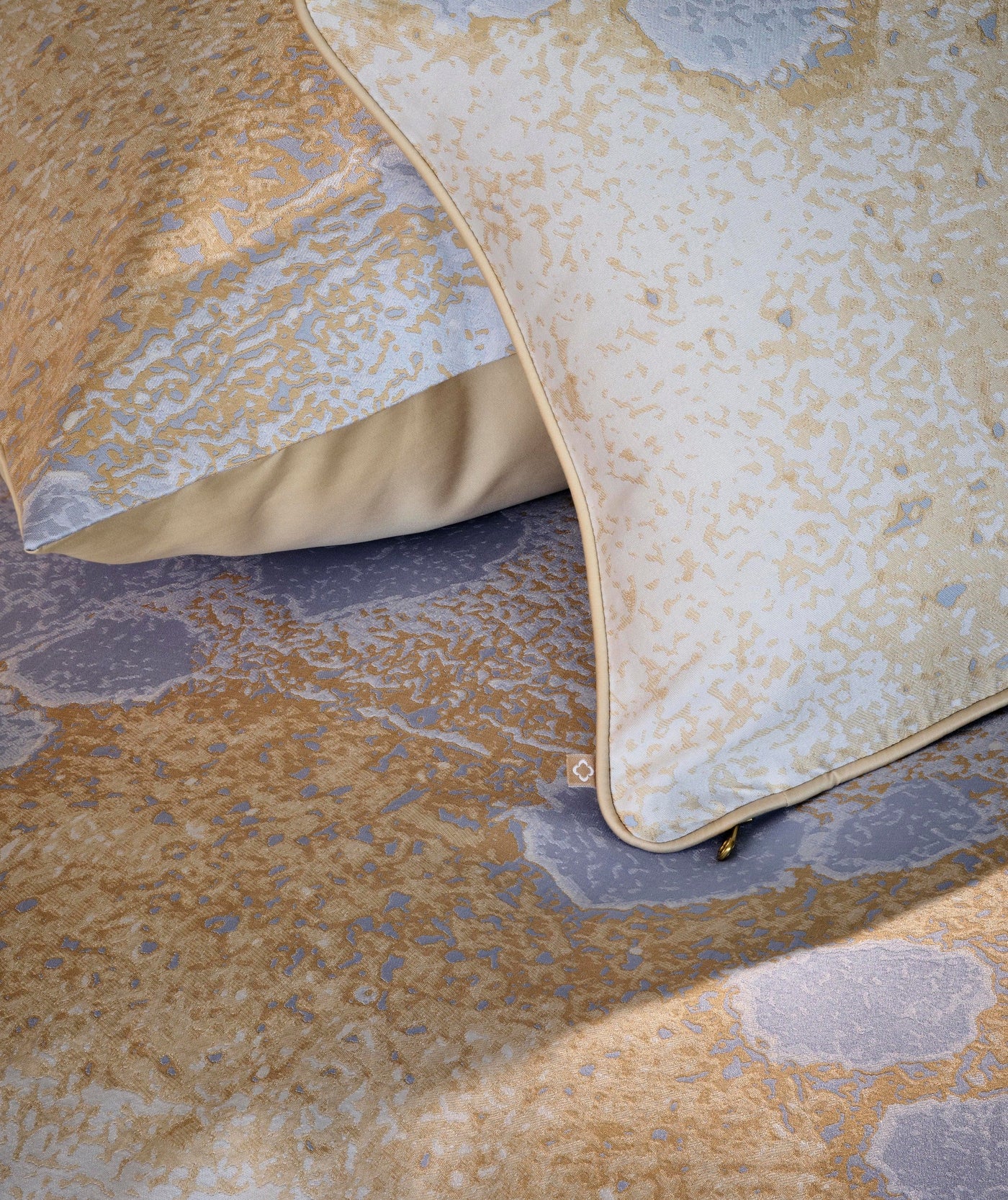 Close-up of two pillows with a textured abstract pattern in gold, ivory, and pale blue. featuring Callisto Pillowcase by Celso de Lemos available at Linen Society.