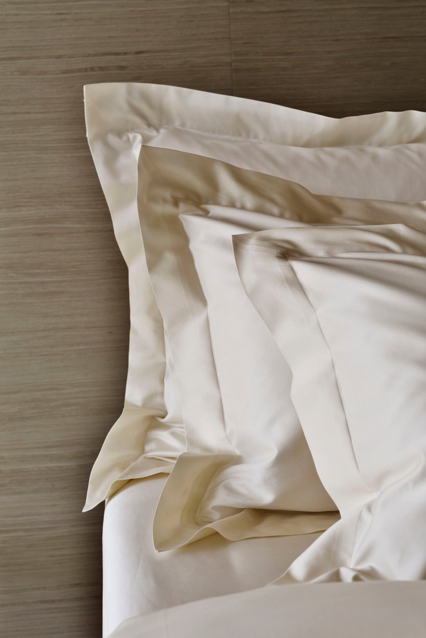 Cream-colored bedding arranged on a wooden surface, featuring Capela Pillowcase by Celso de Lemos available at Linen Society.