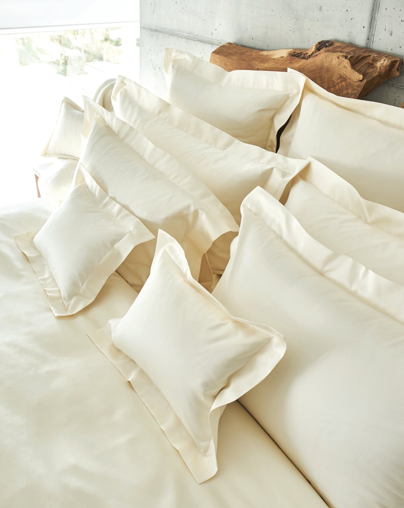 A collection of crisp, creamy white pillowcases are neatly arranged on a bed, featuring the Capela Pillowcase by Celso de Lemos available at Linen Society.