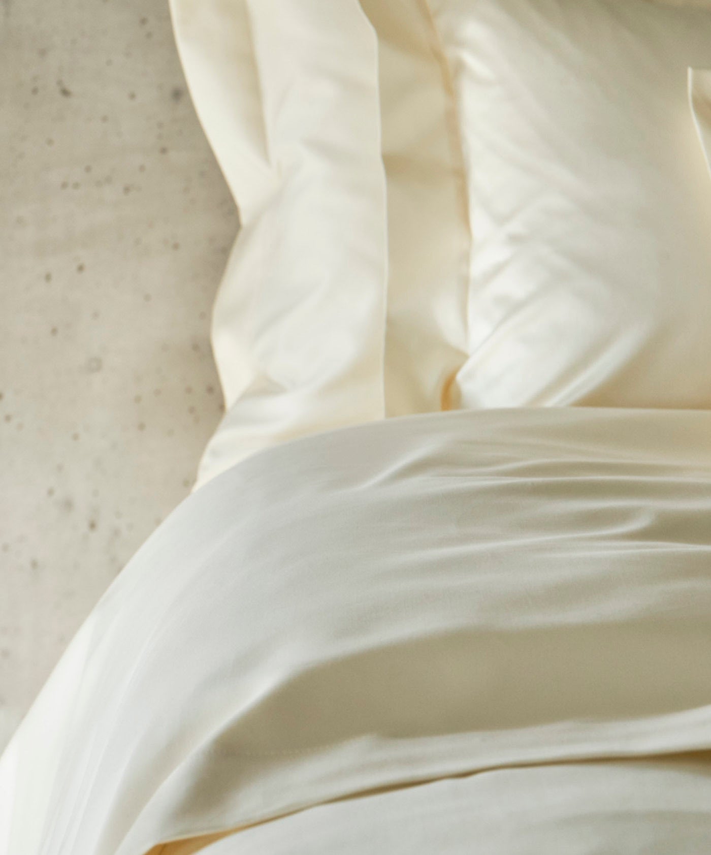Cream colored bedding is artfully arranged on a concrete surface, featuring Capela Pillowcase by Celso de Lemos available at Linen Society.