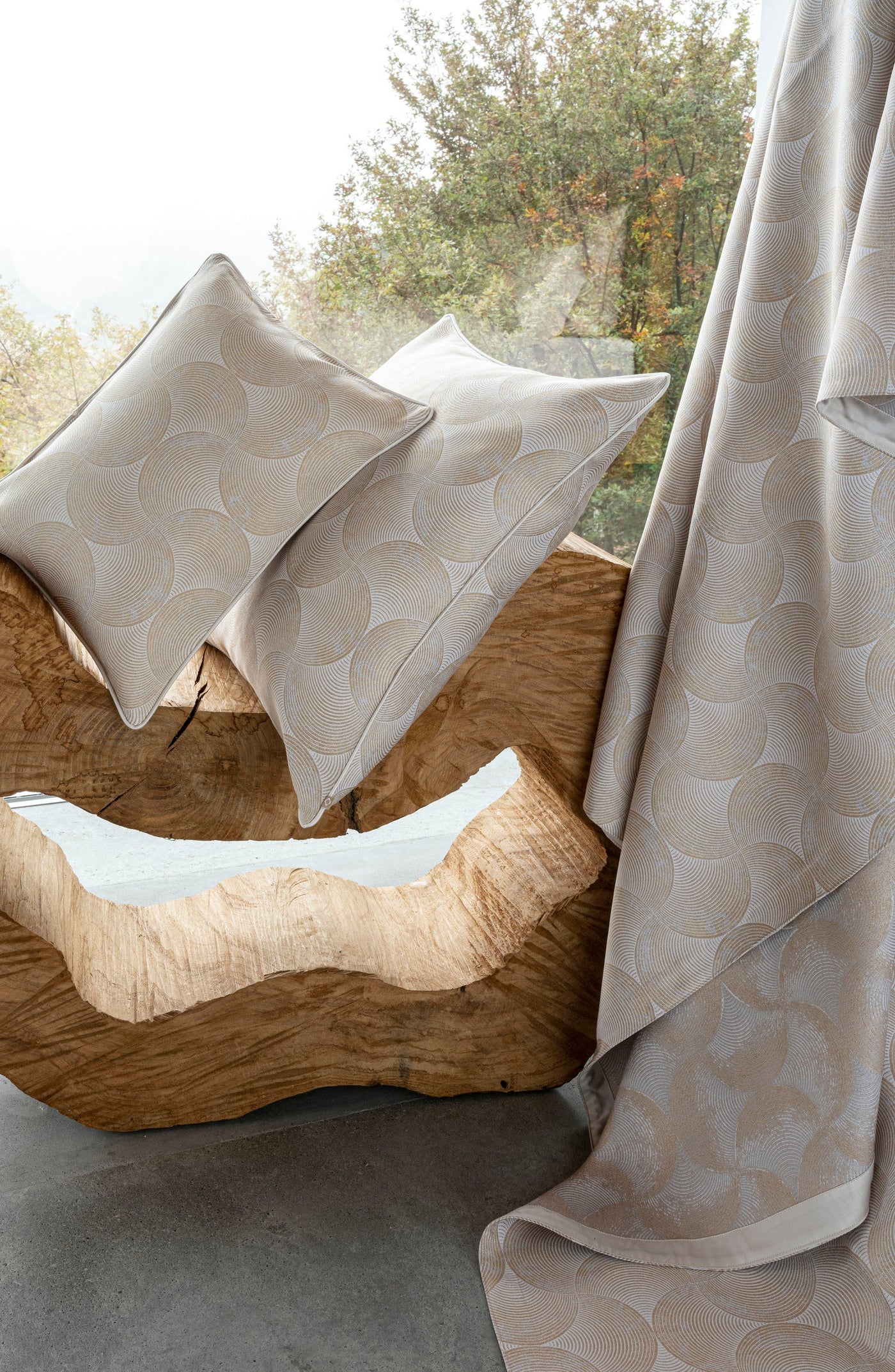 Two neutral-toned pillows with a geometric pattern rest on a wooden sculpture near a window. Featuring Caviar Pillow Covers by Celso de Lemos available at Linen Society.