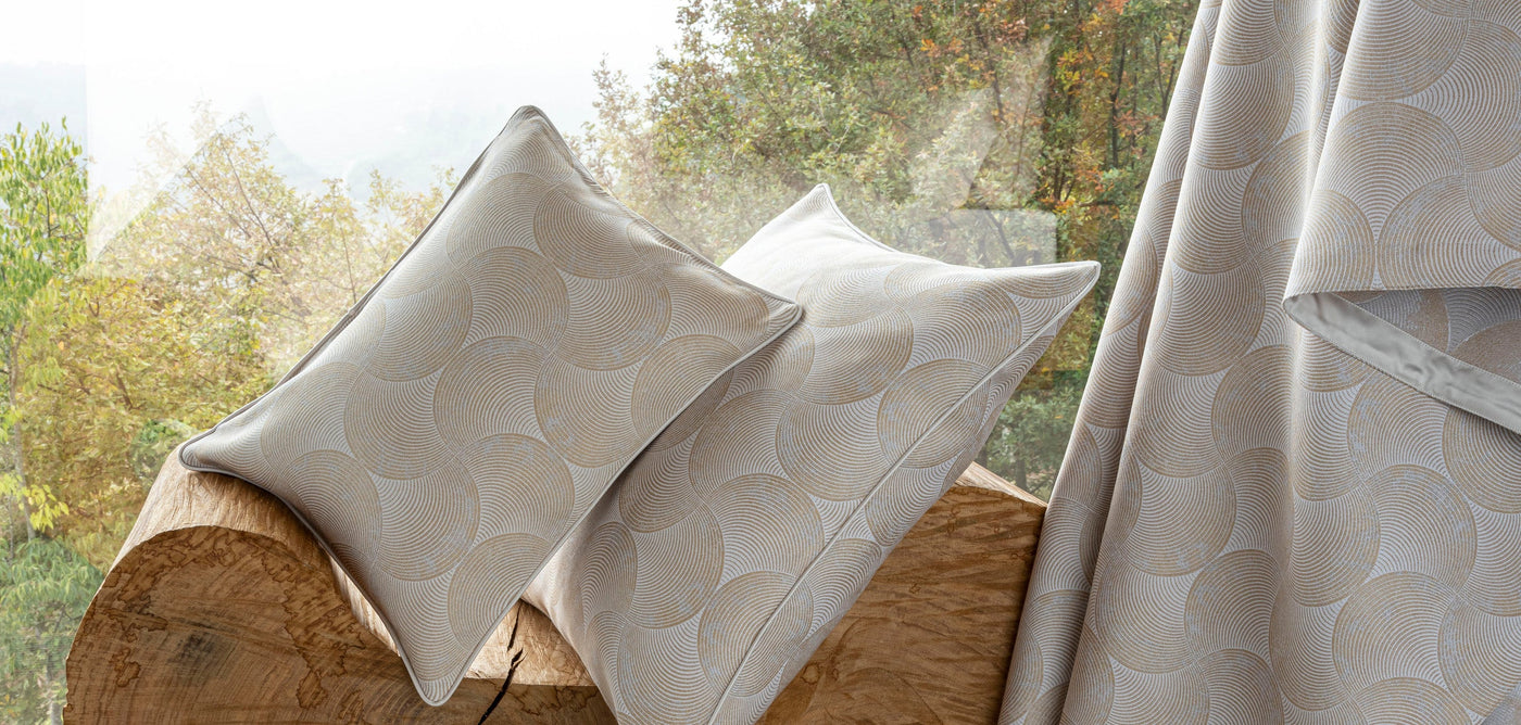Two neutral-toned pillows with a geometric arc pattern rest on a rustic wood surface, featuring Caviar Pillow Cover by Celso de Lemos available at Linen Society.