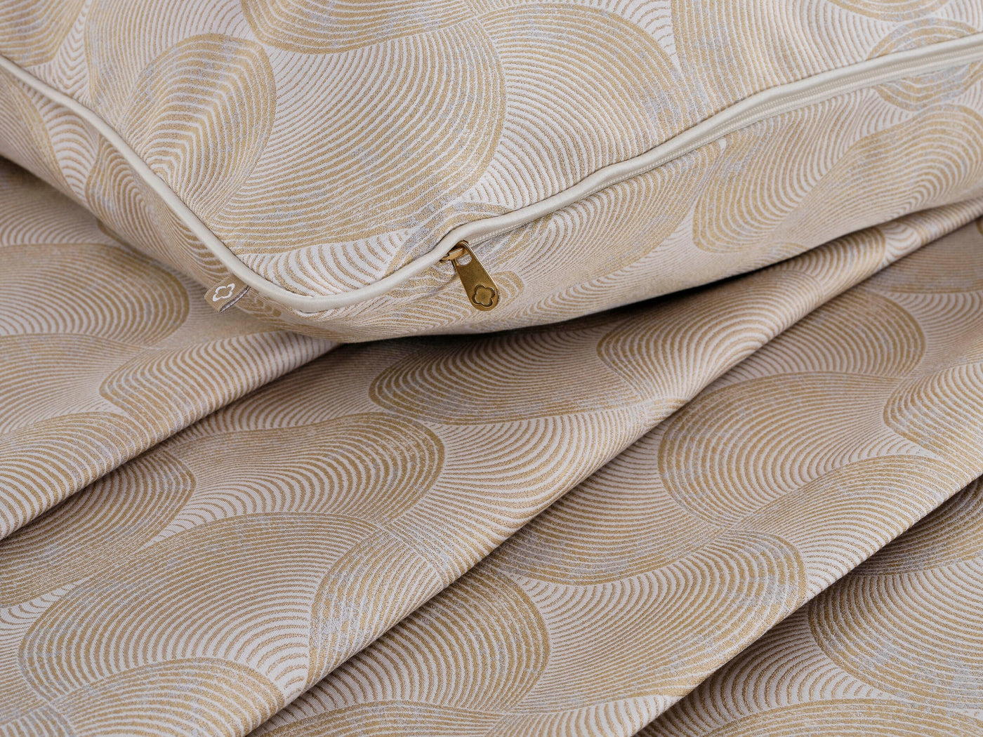Close-up of a textured beige and gold patterned pillow cover with a cream piping and gold zipper, featuring Caviar Pillow Cover by Celso de Lemos available at Linen Society.