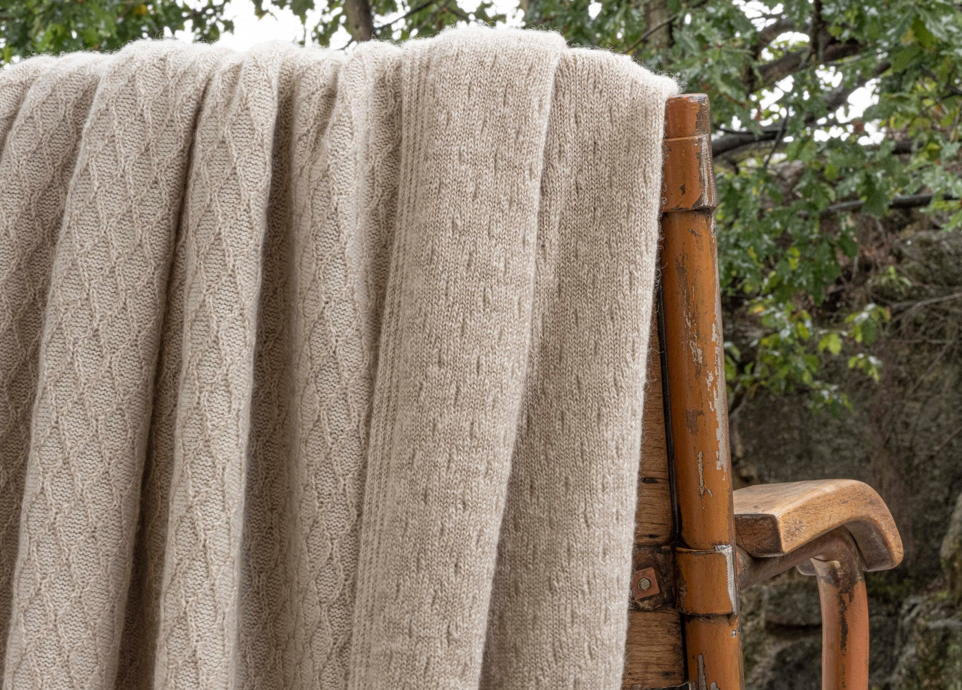 Oatmeal cable-knit throw draped over a bamboo chair, textured diamond pattern visible.