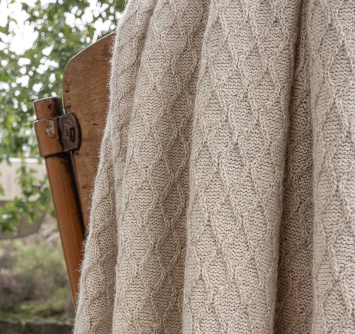 Close-up of Celso de Lemos Cécile throw's oatmeal diamond cable-knit texture draped over a wooden chair.