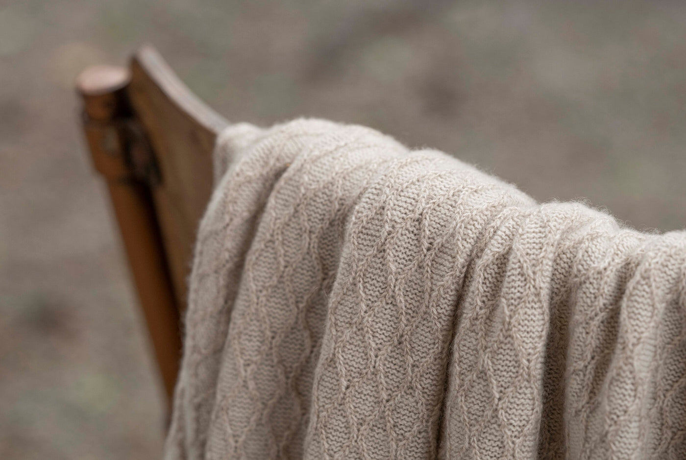 Close-up of Celso de Lemos Cécile throw's diamond cable-knit texture in oatmeal, draped over wooden chair.