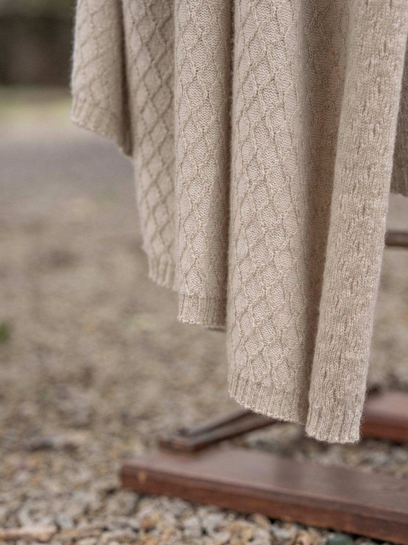 Close-up of oatmeal cable-knit texture and ribbed hem on Cécile throw draped outdoors.