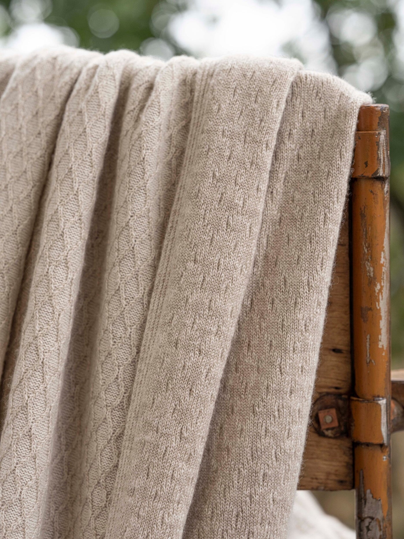 Close-up of oatmeal cable-knit throw draped over a rustic bamboo chair.