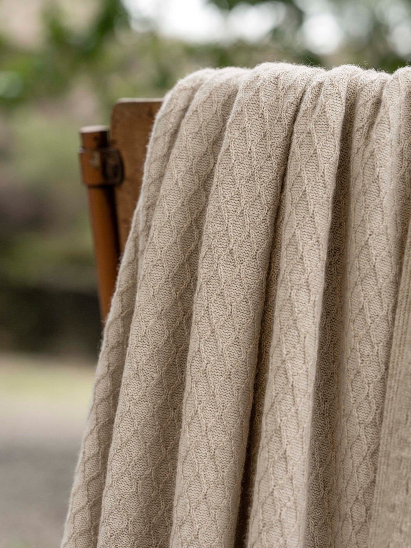 Close-up of oatmeal cable-knit throw draped over a wooden chair back outdoors.