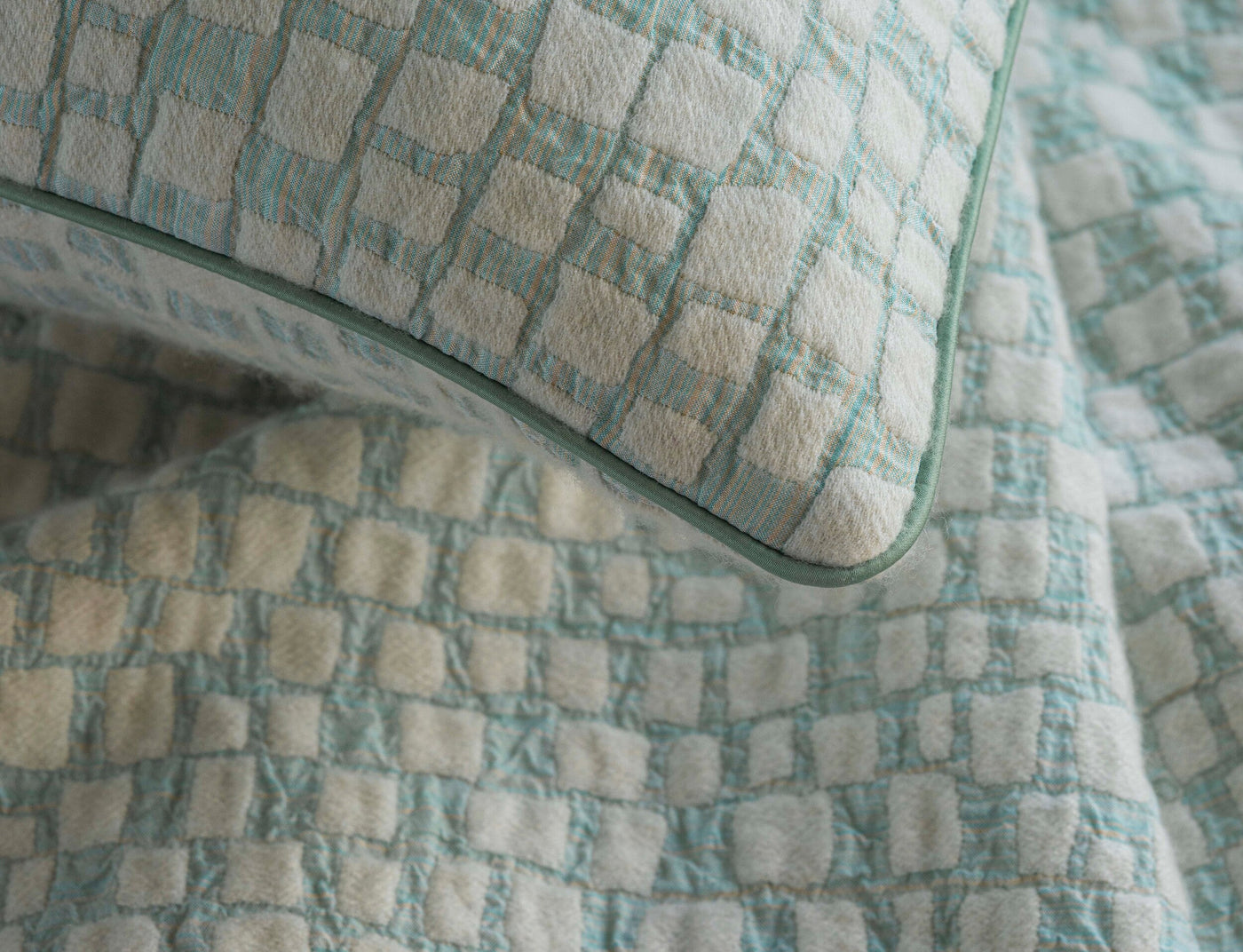 A close-up shot of a textured pillow and draped fabric in a light blue and cream checkered pattern, featuring City Pillow Cover by Celso de Lemos available at Linen Society.