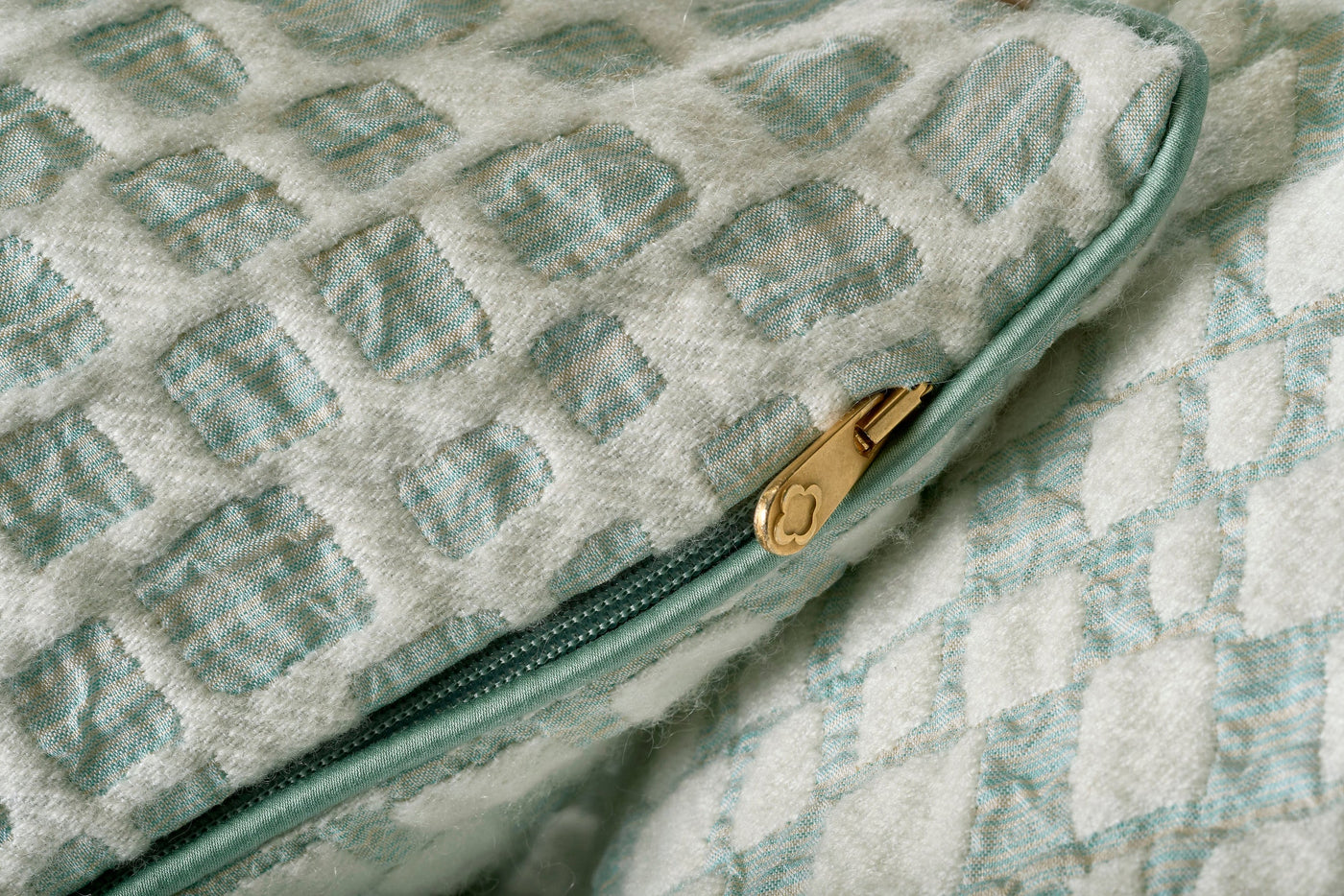 Close-up of a textured pillow cover with a diamond pattern in cream and light blue, featuring a gold zipper, Pillow Cover by Celso de Lemos available at Linen Society.