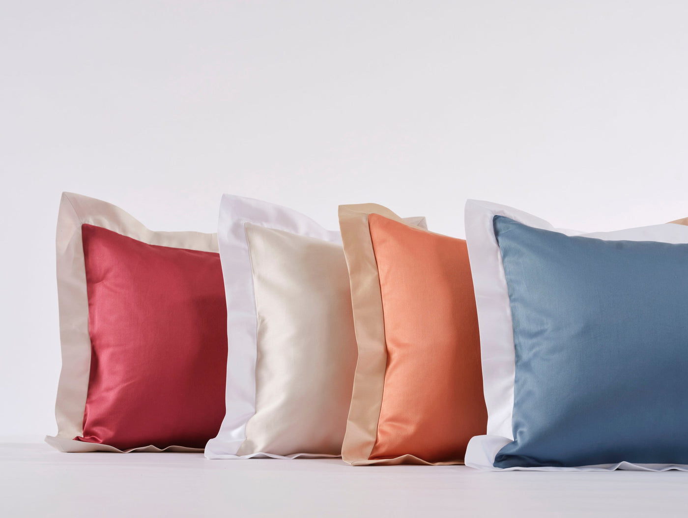 A row of four colorful pillowcases in red, cream, coral, and blue, featuring Emma Pillowcase by Celso de Lemos available at Linen Society.