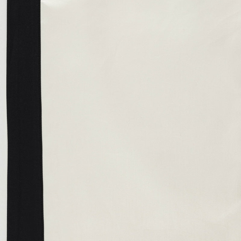 A close-up of a creamy white pillowcase with a black stripe along the left edge, featuring Emma Pillowcase by Celso de Lemos available at Linen Society.
