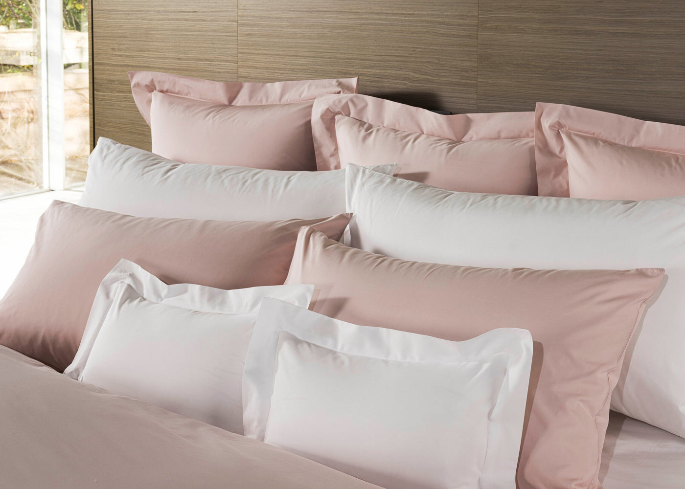 A neatly made bed displays layered pillows in soft blush and crisp white, featuring Estrela Pillowcase by Celso de Lemos available at Linen Society.