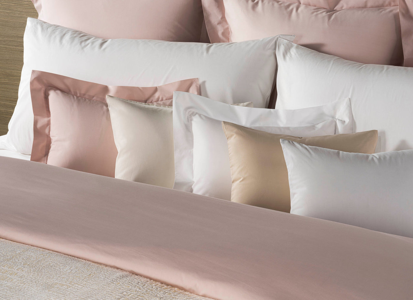 A neat stack of pillows in blush pink, cream, and white, arranged on a bed featuring Estrela Pillowcase by Celso de Lemos available at Linen Society.