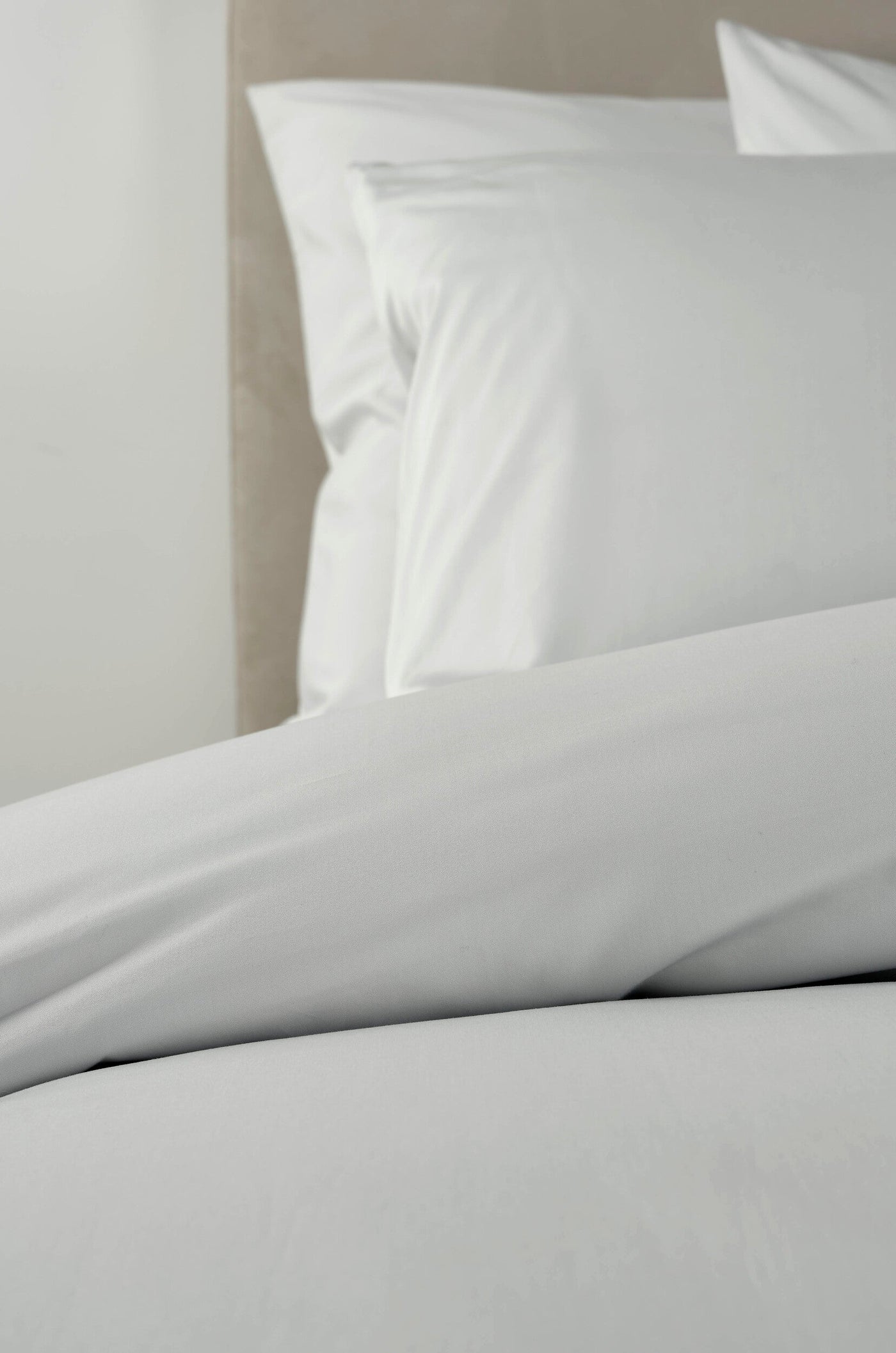 Crisp white bedding is neatly arranged against a neutral headboard. featuring Estrela Pillowcase by Celso de Lemos available at Linen Society.