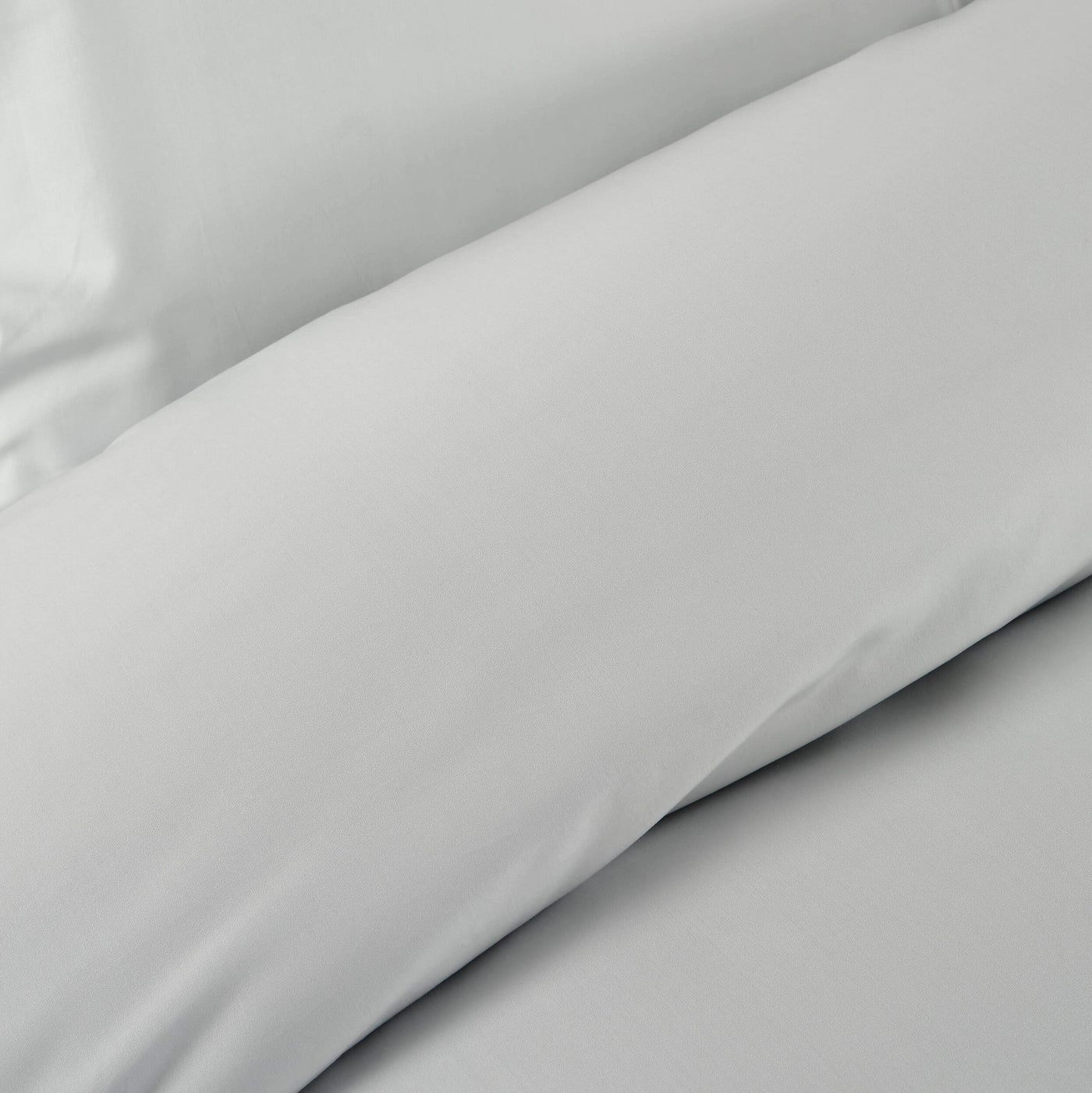 A close-up of folded pale grey bedding, showing a subtle texture featuring Estrela Pillowcase by Celso de Lemos available at Linen Society.