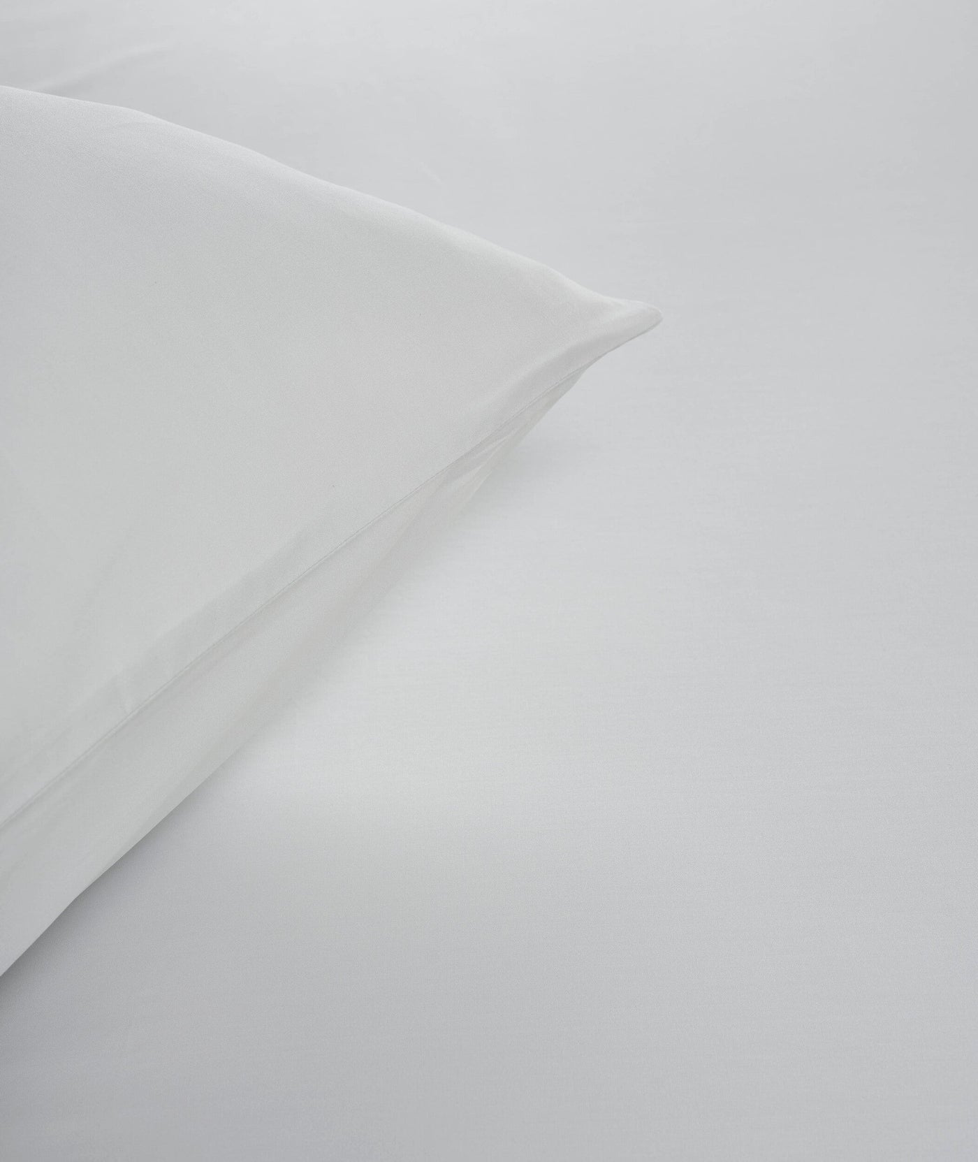 Crisp white fabric is folded to show the subtle texture, featuring Estrela Pillowcase by Celso de Lemos available at Linen Society.