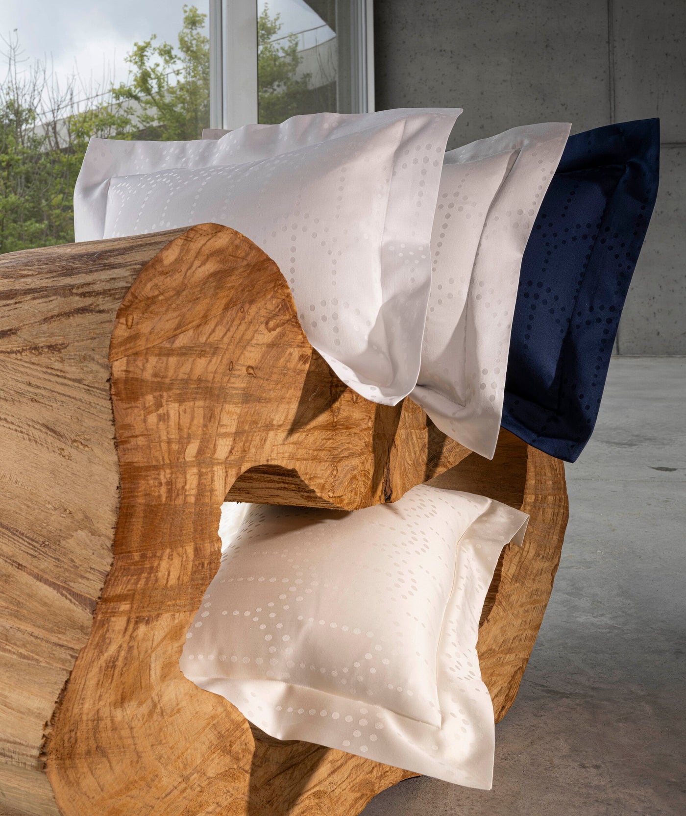 Pillowcases in white, cream, and navy blue with a subtle dot pattern are arranged on a wooden surface. featuring Evora Pillowcase by Celso de Lemos available at Linen Society.