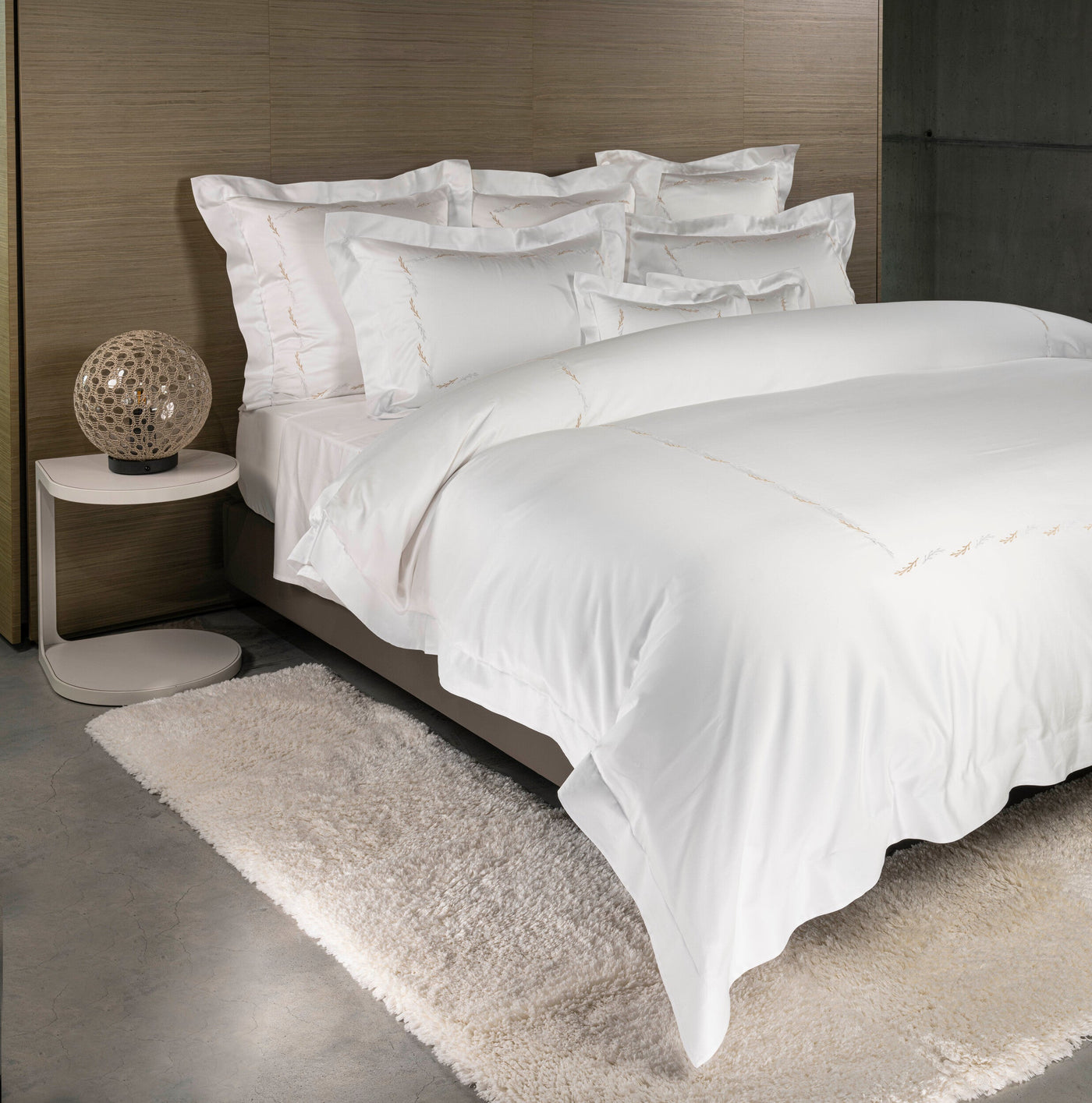 A neatly made bed with crisp white bedding, featuring delicate embroidered leaf motifs, displayed in a modern bedroom setting. featuring Fern Pillowcase by Celso de Lemos available at Linen Society.