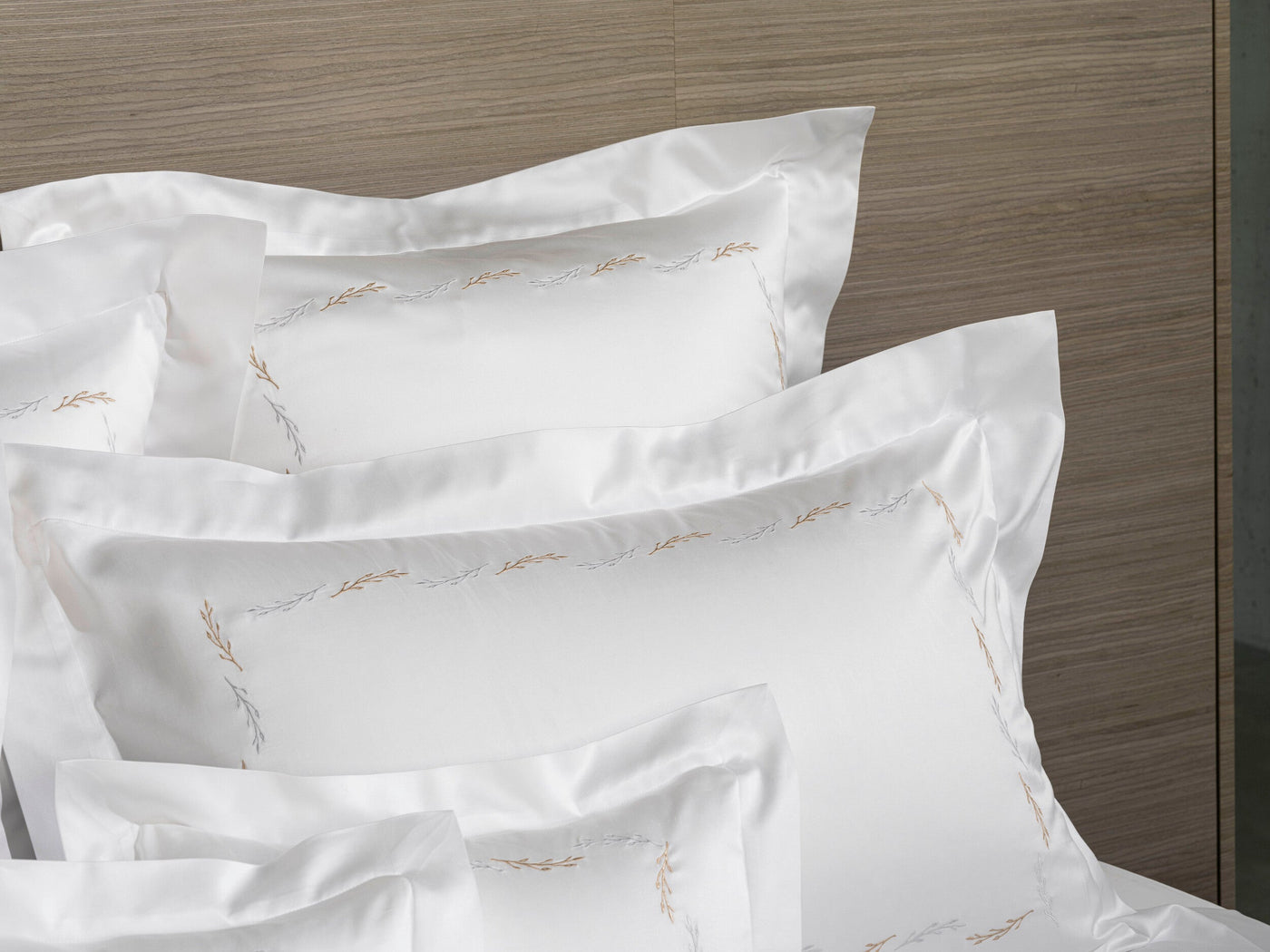 A stack of white pillowcases with a subtle embroidered leaf pattern in gold and silver, featuring Fern Pillowcase by Celso de Lemos available at Linen Society.