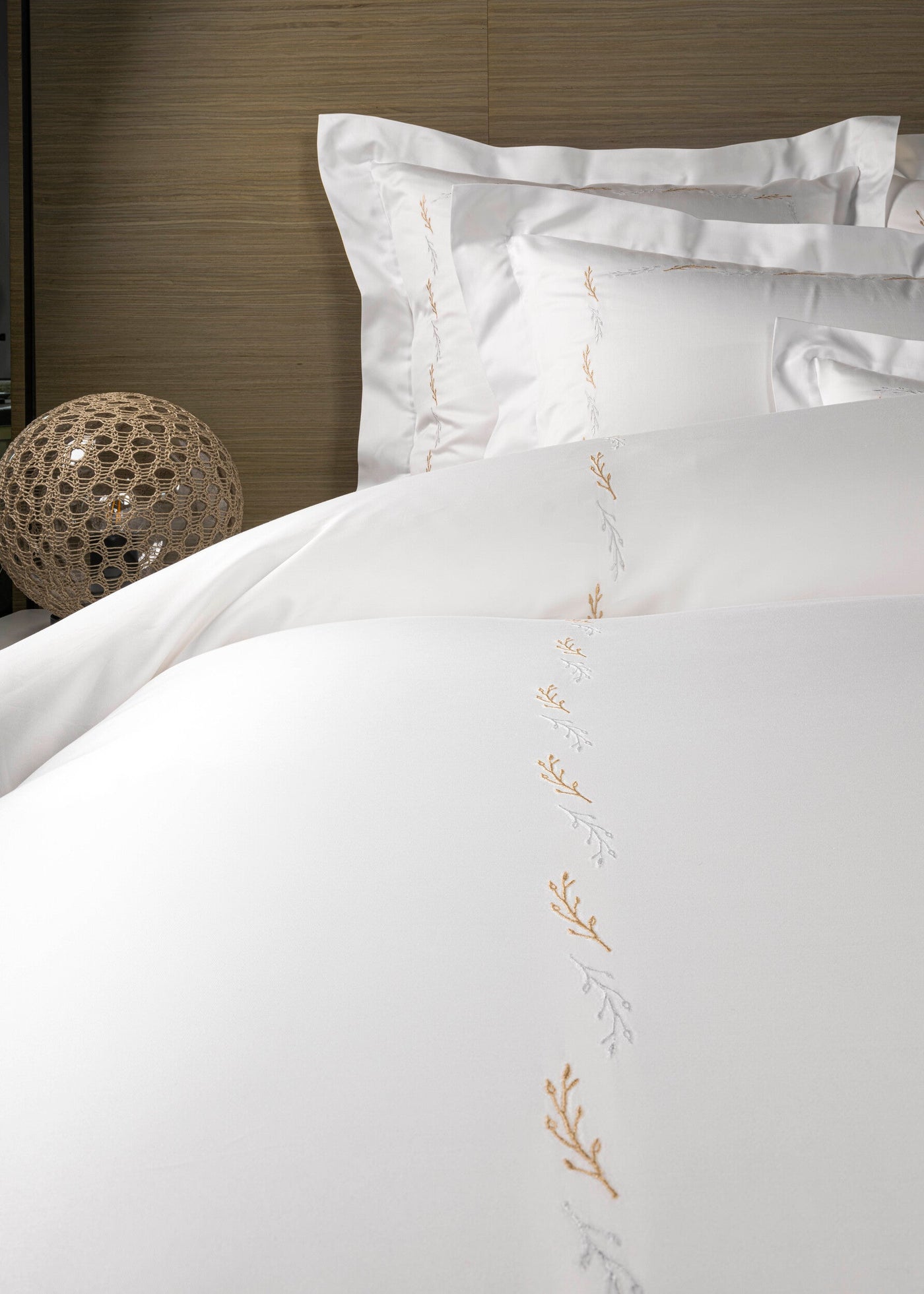 Crisp white bedding with delicate gold and silver embroidered leaf sprigs arranged vertically, featuring Fern Pillowcase by Celso de Lemos available at Linen Society.