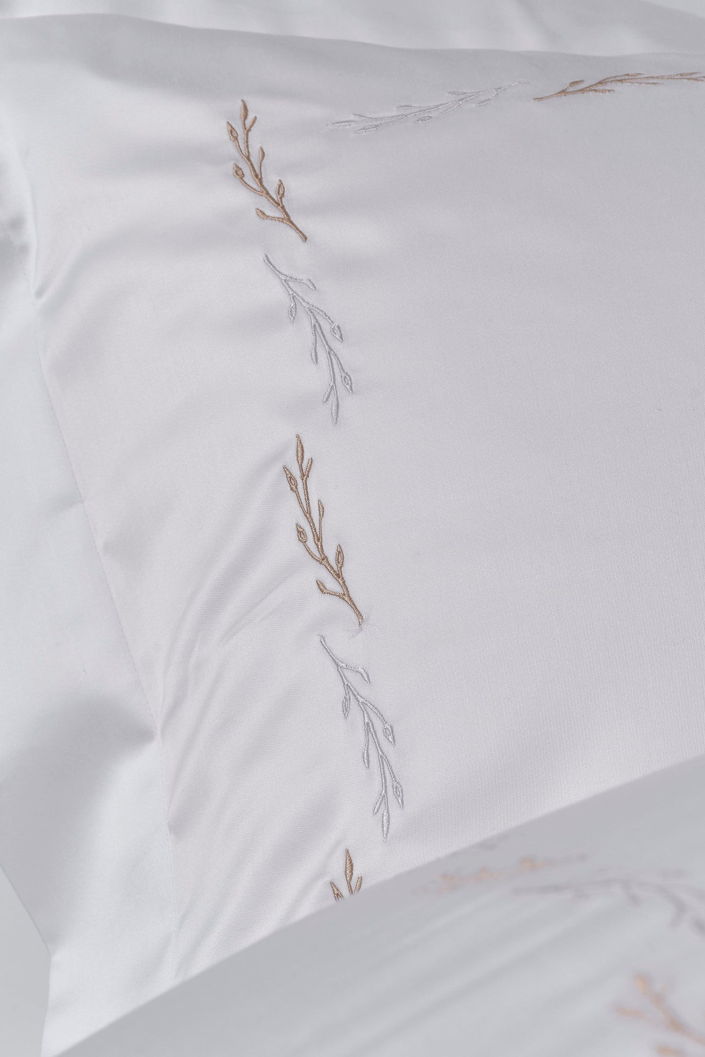 A white pillowcase is shown with delicate embroidery of branches in gold and silver thread, featuring Fern Pillowcase by Celso de Lemos available at Linen Society.
