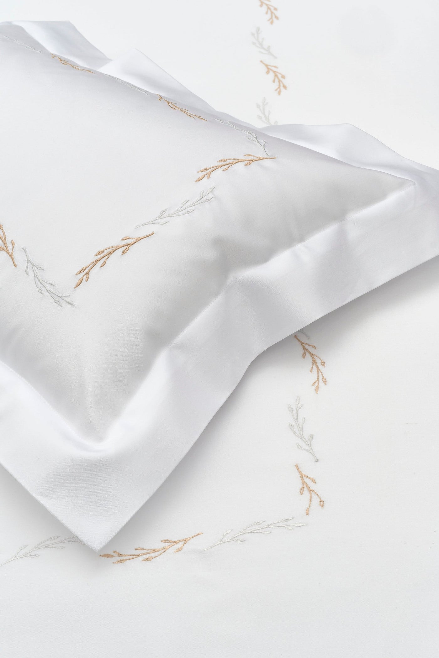 White pillowcase with embroidered beige and silver branches, featuring the Fern Pillowcase by Celso de Lemos available at Linen Society.