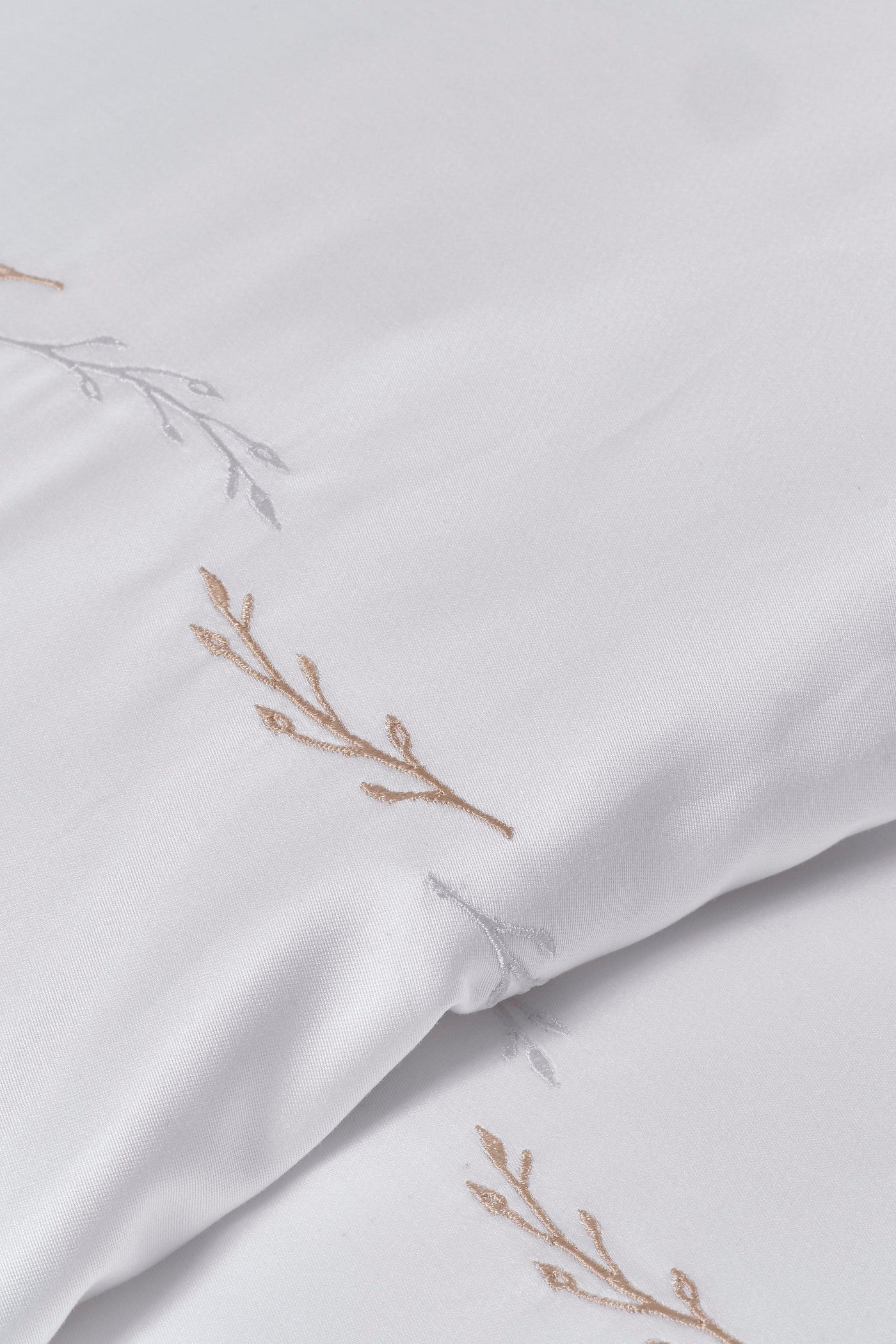 White fabric with delicate embroidered branch motifs in tan and pale grey, featuring Fern Pillowcase by Celso de Lemos available at Linen Society.