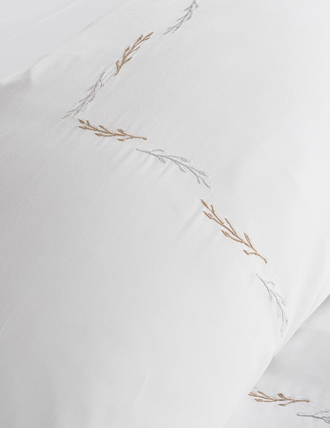 White pillowcase with delicate gold and silver embroidered branches, featuring Fern Pillowcase by Celso de Lemos available at Linen Society.