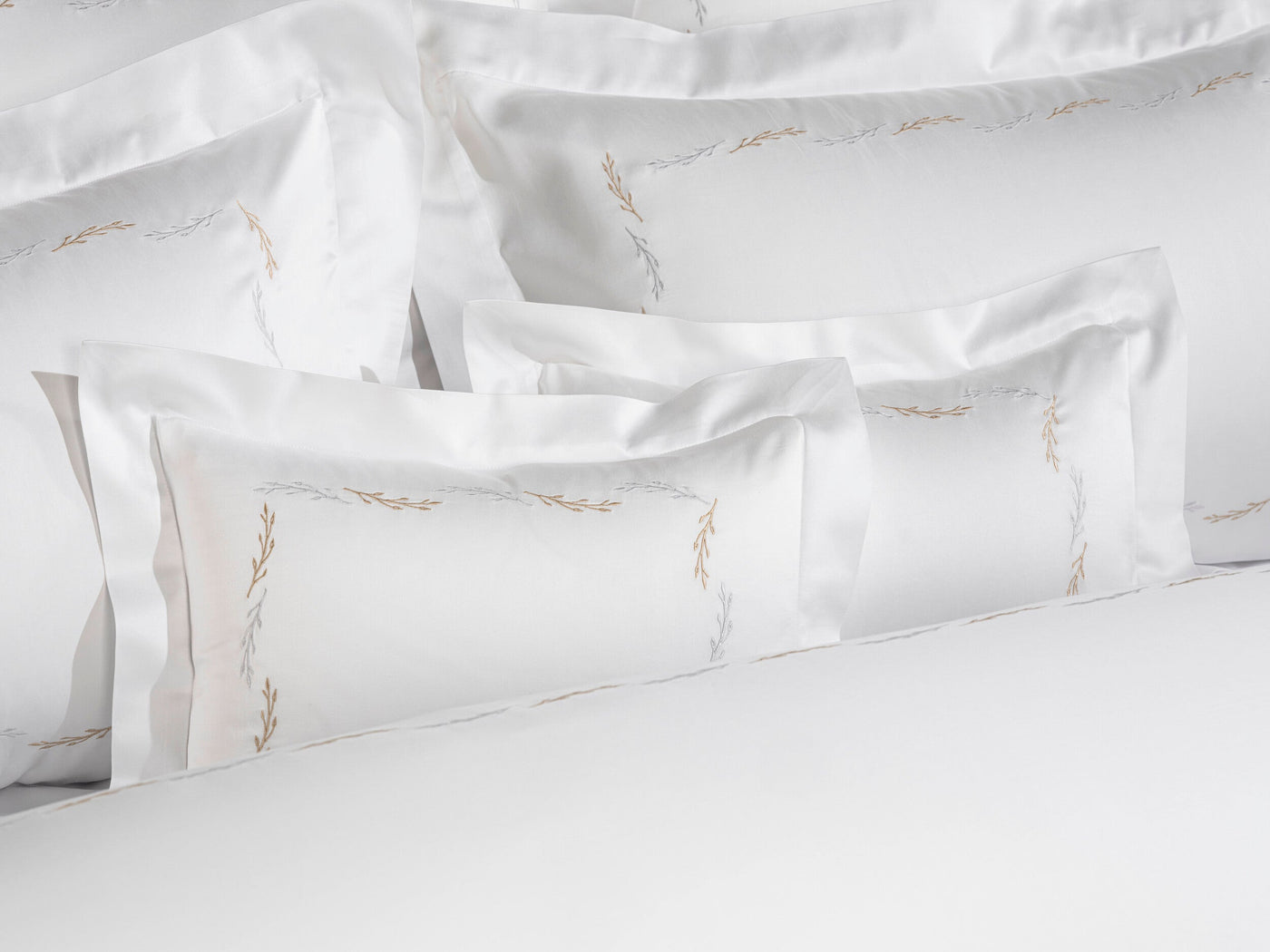 Close-up view of neatly folded white pillowcases with delicate embroidered branches in gold and silver, featuring Fern Pillowcase by Celso de Lemos available at Linen Society.