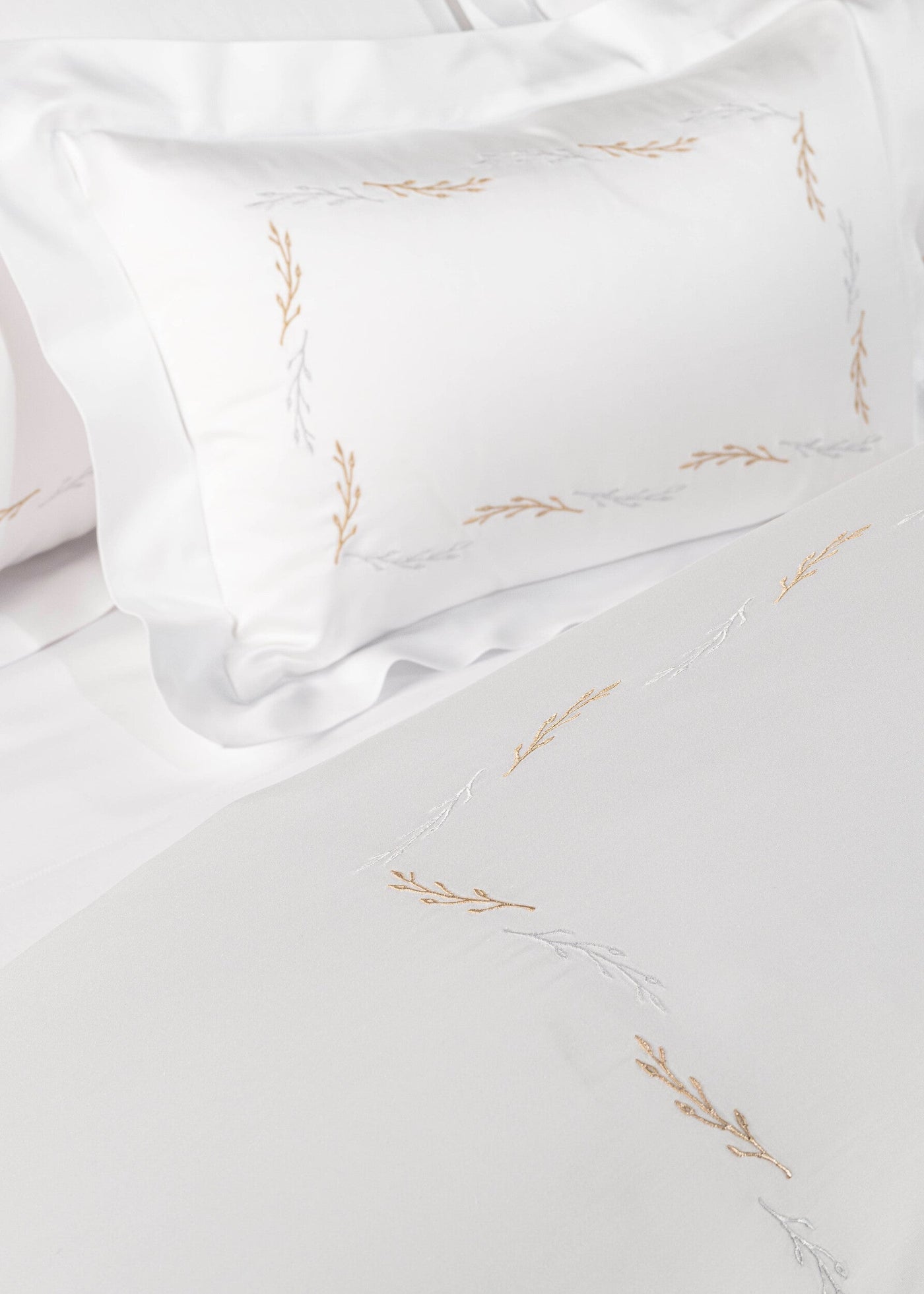 White bedding with embroidered gold and silver branches, featuring Fern Pillowcase by Celso de Lemos available at Linen Society.