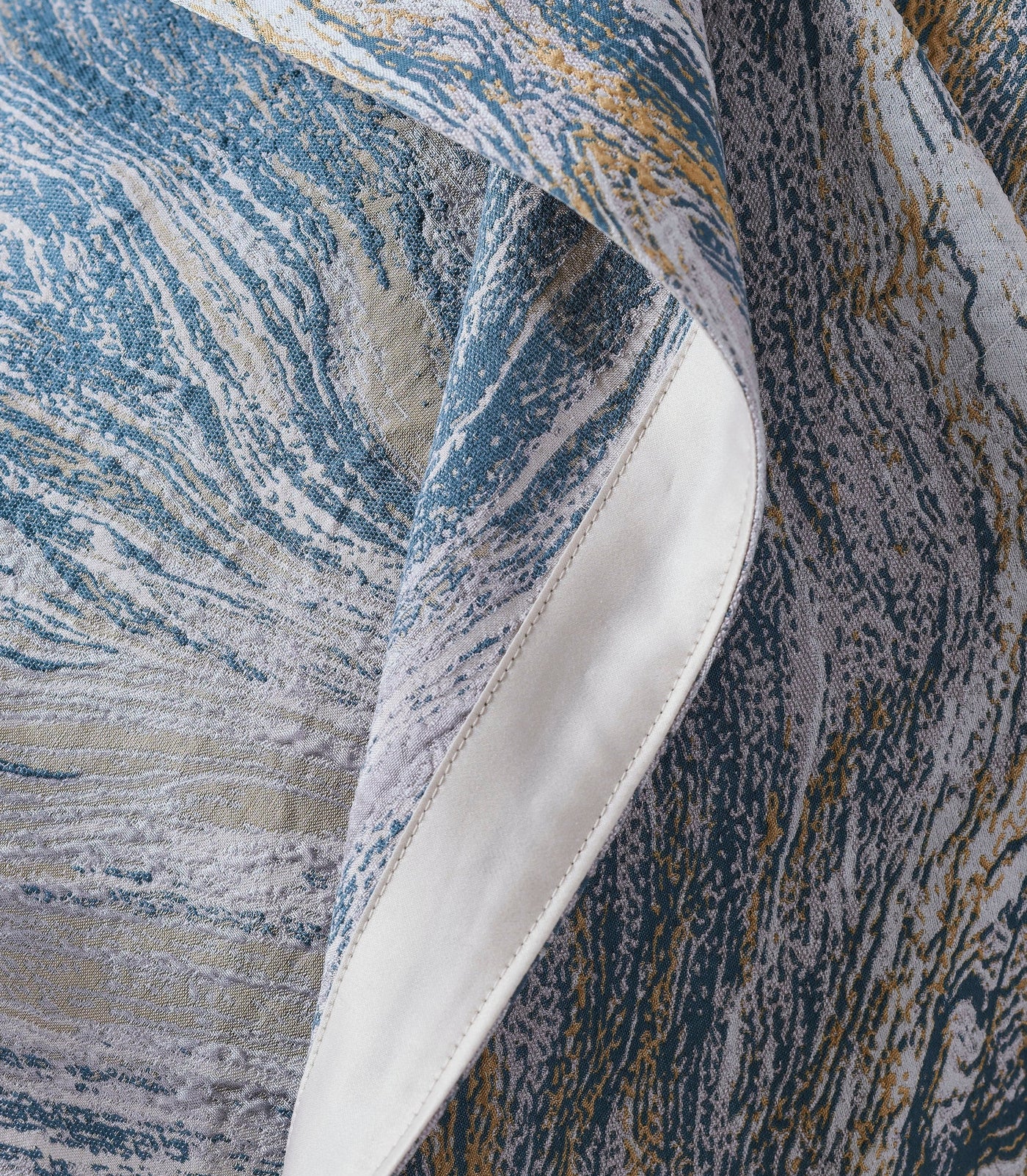 Close-up of a textured fabric with a swirling blue, grey, and gold abstract pattern, featuring Filigrane Bed Cover by Celso de Lemos available at Linen Society.