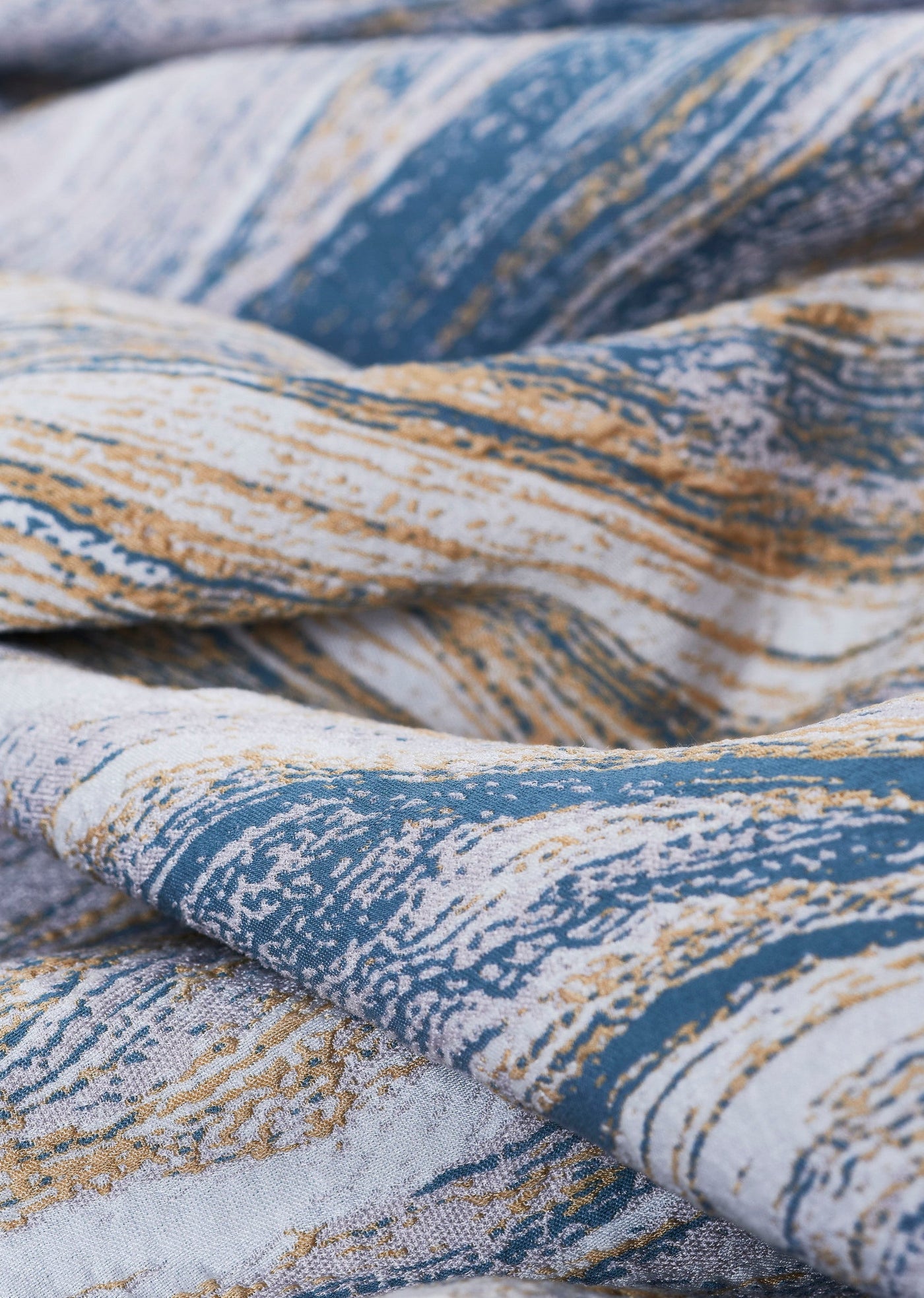 Textured fabric with abstract streaks of blue, gold, and white, featuring Filigrane Pillow Cover by Celso de Lemos available at Linen Society.
