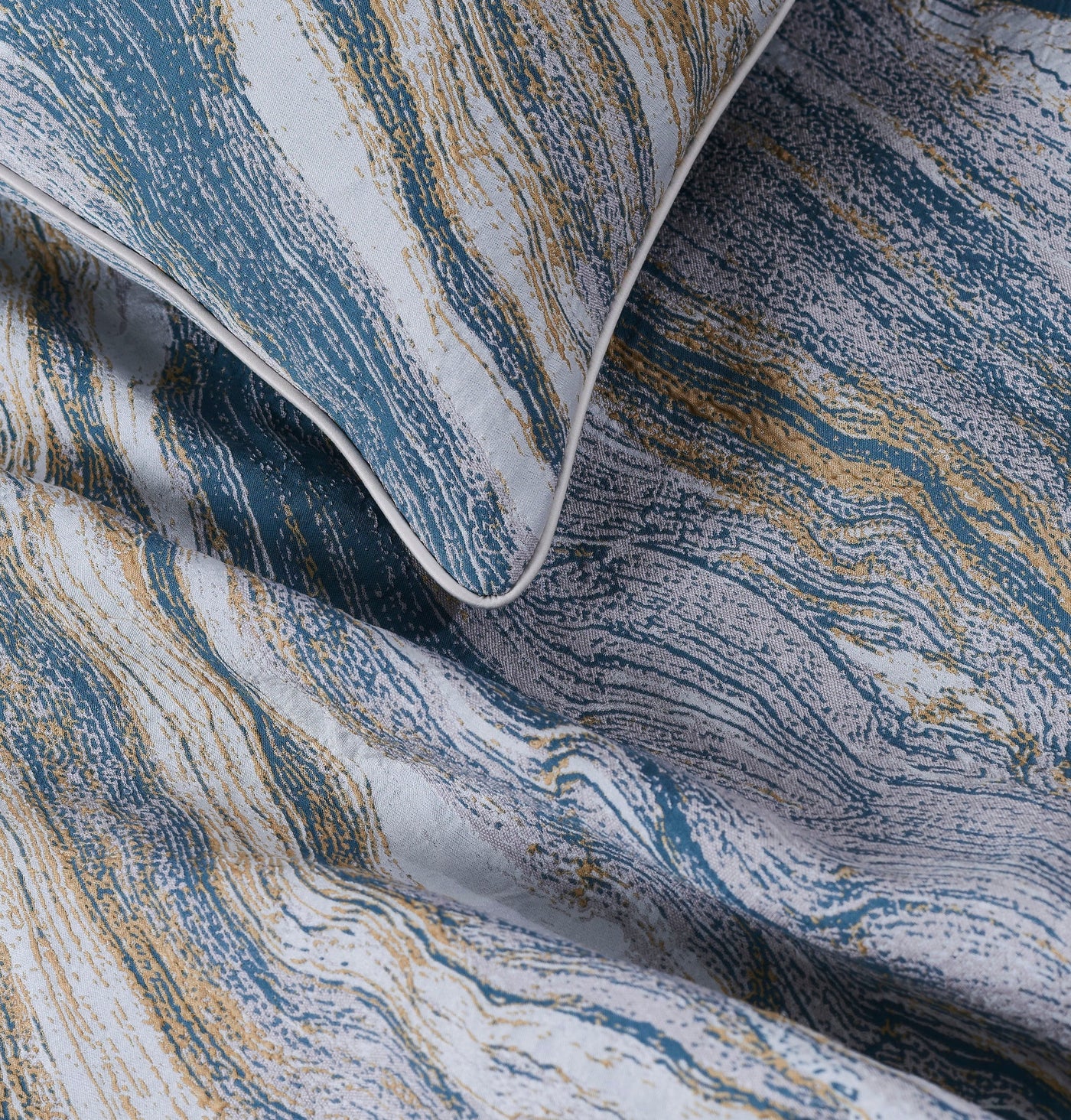Close-up of a pillow with a textured, abstract pattern in blue, gold, and off-white, featuring the Filigrane Pillow Cover by Celso de Lemos available at Linen Society.