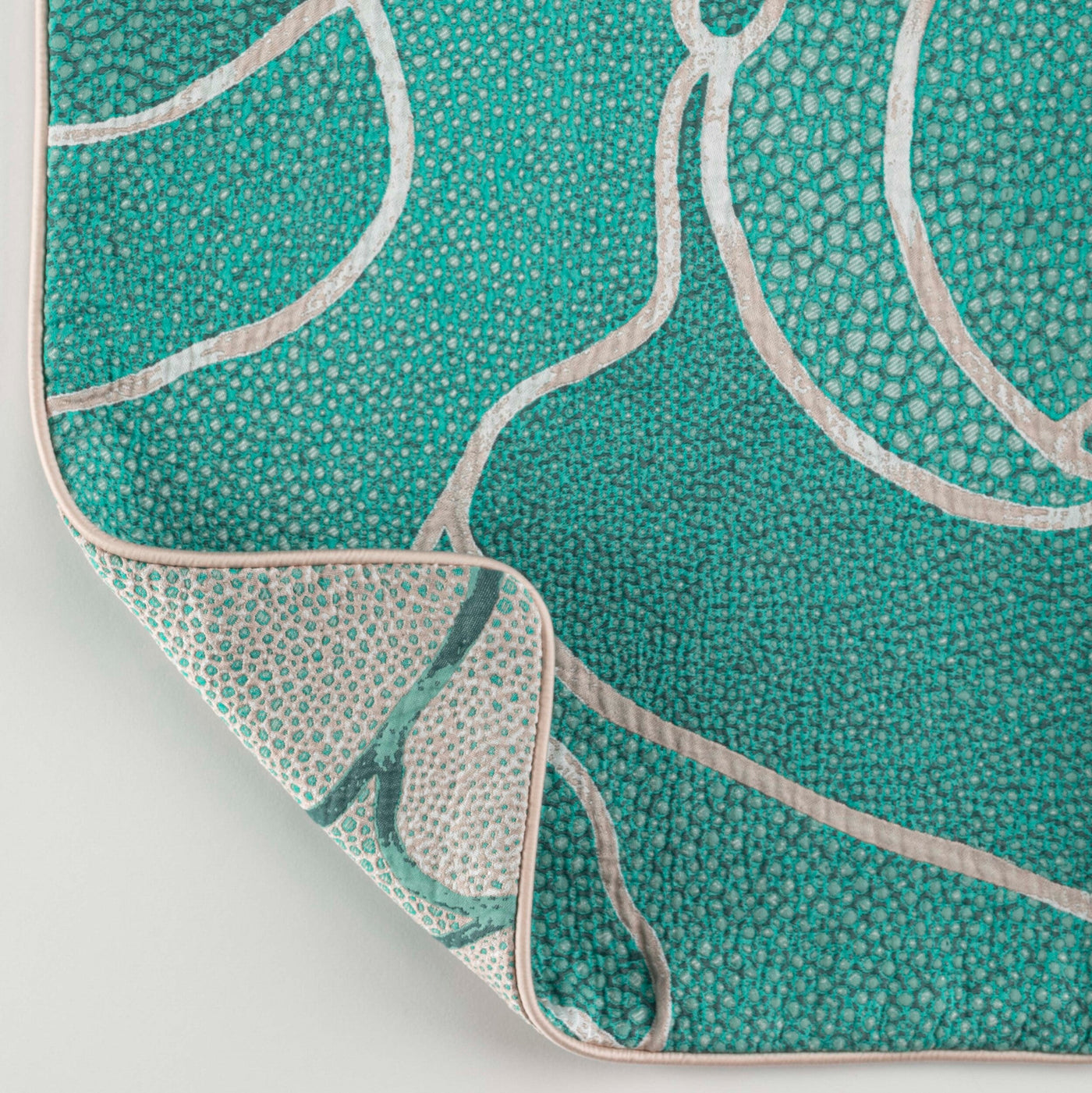 Close-up view of a teal textured fabric with an abstract pattern and cream piping, featuring Funchal Pillow Cover by Celso de Lemos available at Linen Society.
