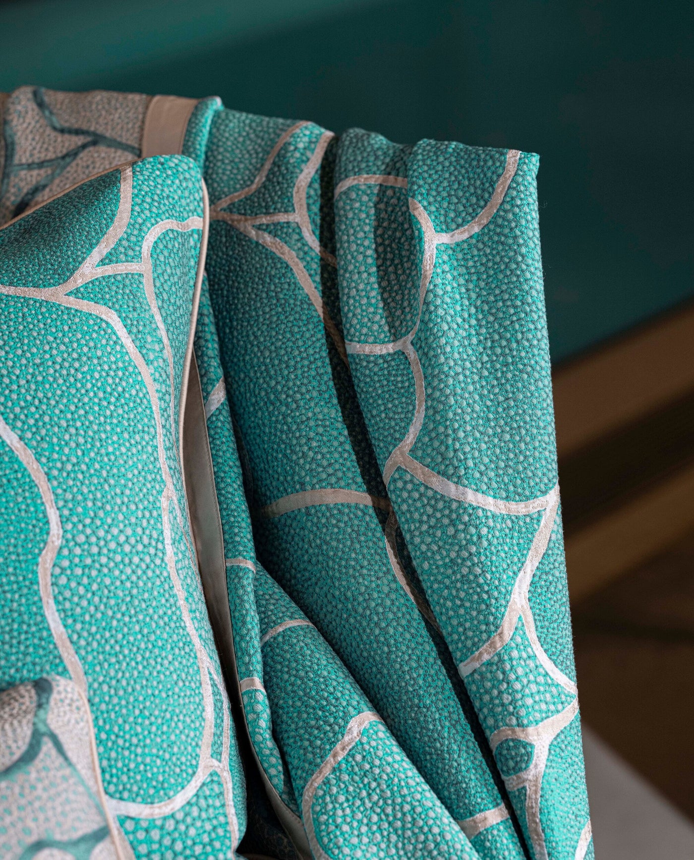 Close-up of draped turquoise textured fabric with a silver geometric pattern, featuring Funchal Pillow Cover by Celso de Lemos available at Linen Society.
