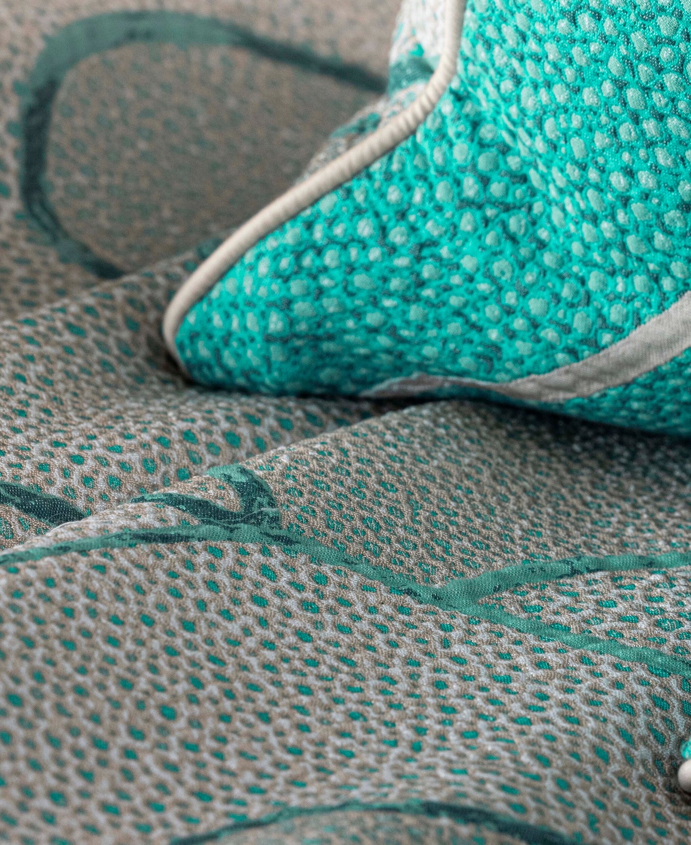 Close-up of a textured pillow with a teal woven pattern and beige trim, set against a matching textured fabric. featuring Funchal Pillow Cover by Celso de Lemos available at Linen Society.