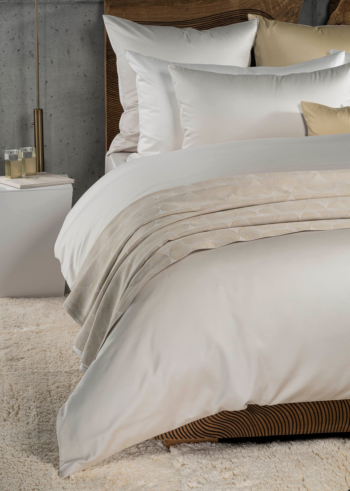 A close-up of a bed with white sheets and pillows, featuring a cream throw with a circular pattern, featuring Gemini Pillowcase by Celso de Lemos available at Linen Society.