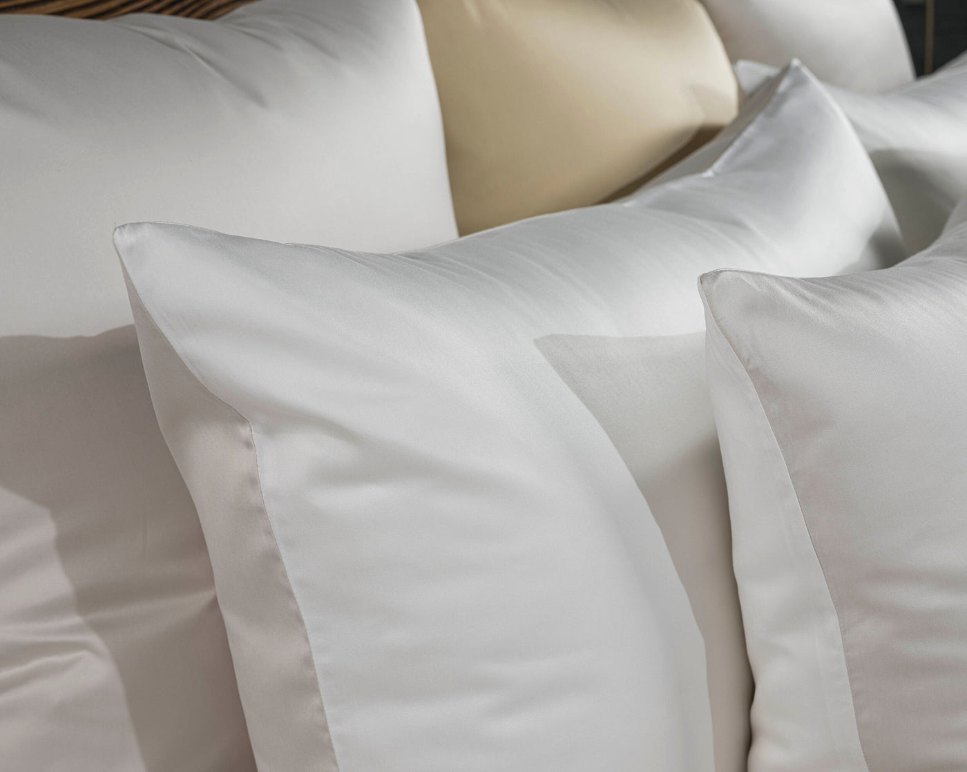 A stack of crisp white and pale yellow pillows are arranged in a close-up shot, featuring Gemini Pillowcase by Celso de Lemos available at Linen Society.