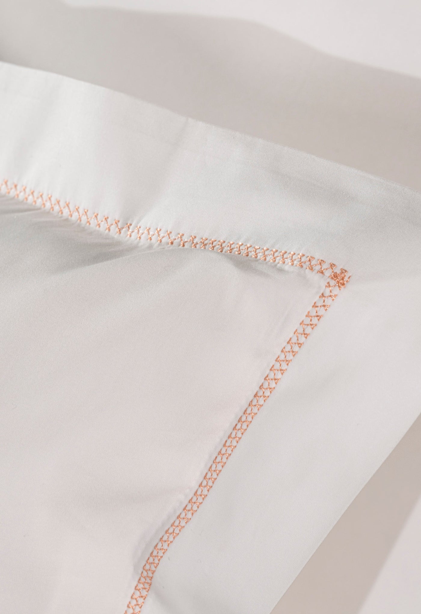 Close-up on white fabric with delicate coral stitching, featuring Ivy Pillowcase by Celso de Lemos available at Linen Society.