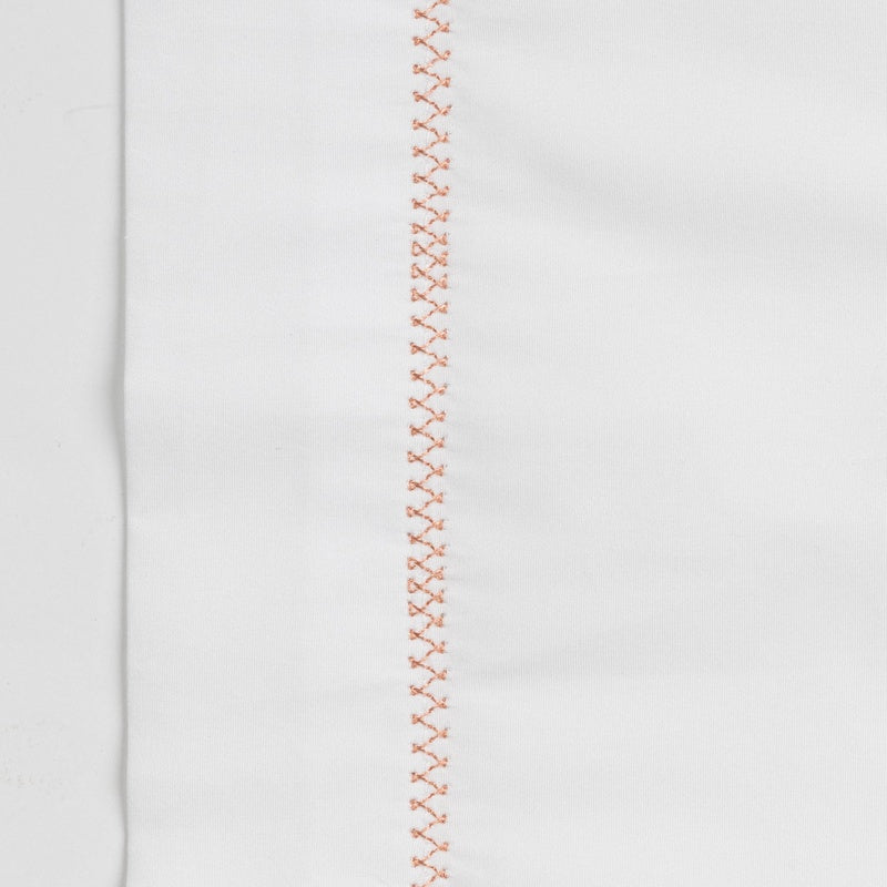 White textile with delicate copper stitching along one edge, featuring Ivy Pillowcase by Celso de Lemos available at Linen Society.