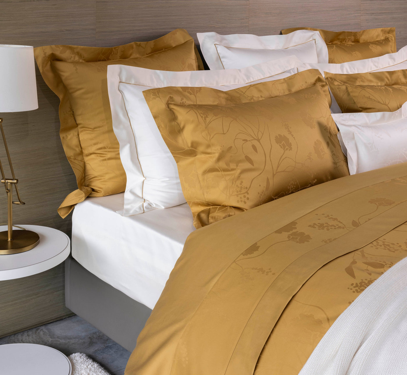 Gold pillowcases with subtle floral pattern and crisp white sheets displayed on a bed, featuring Jardim Pillowcase by Celso de Lemos available at Linen Society.