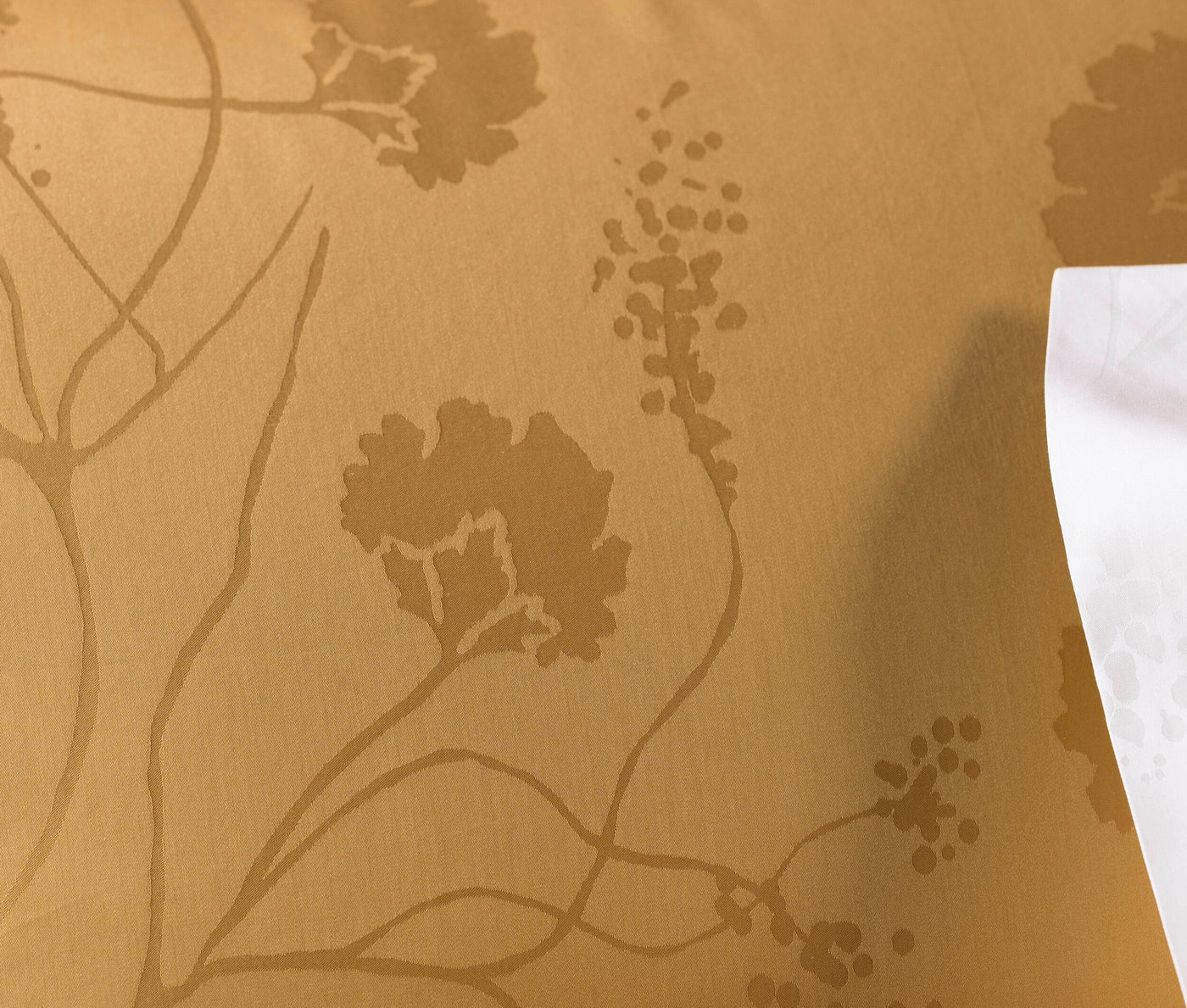 A close-up shows a golden fabric with a subtle floral vine pattern, featuring Pillowcase by Celso de Lemos available at Linen Society.