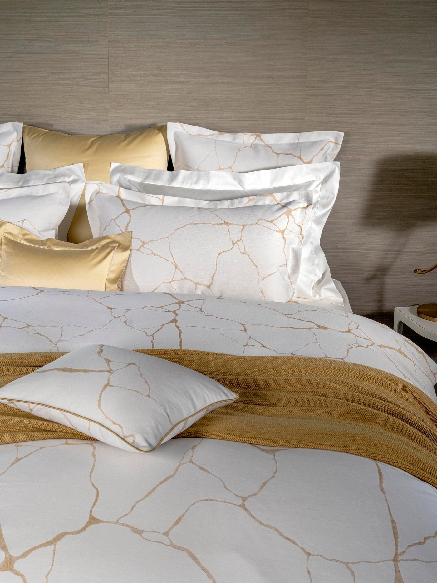 A bed dressed in white bedding with a gold crackle pattern and golden accent pillows, featuring Jessie Pillowcase by Celso de Lemos available at Linen Society.