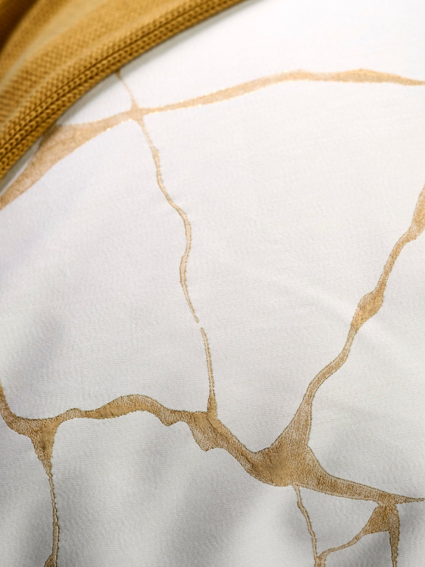 Close-up of white textile with gold Kintsugi-inspired pattern and a mustard yellow textured border, featuring Jessie Pillowcase by Celso de Lemos available at Linen Society.