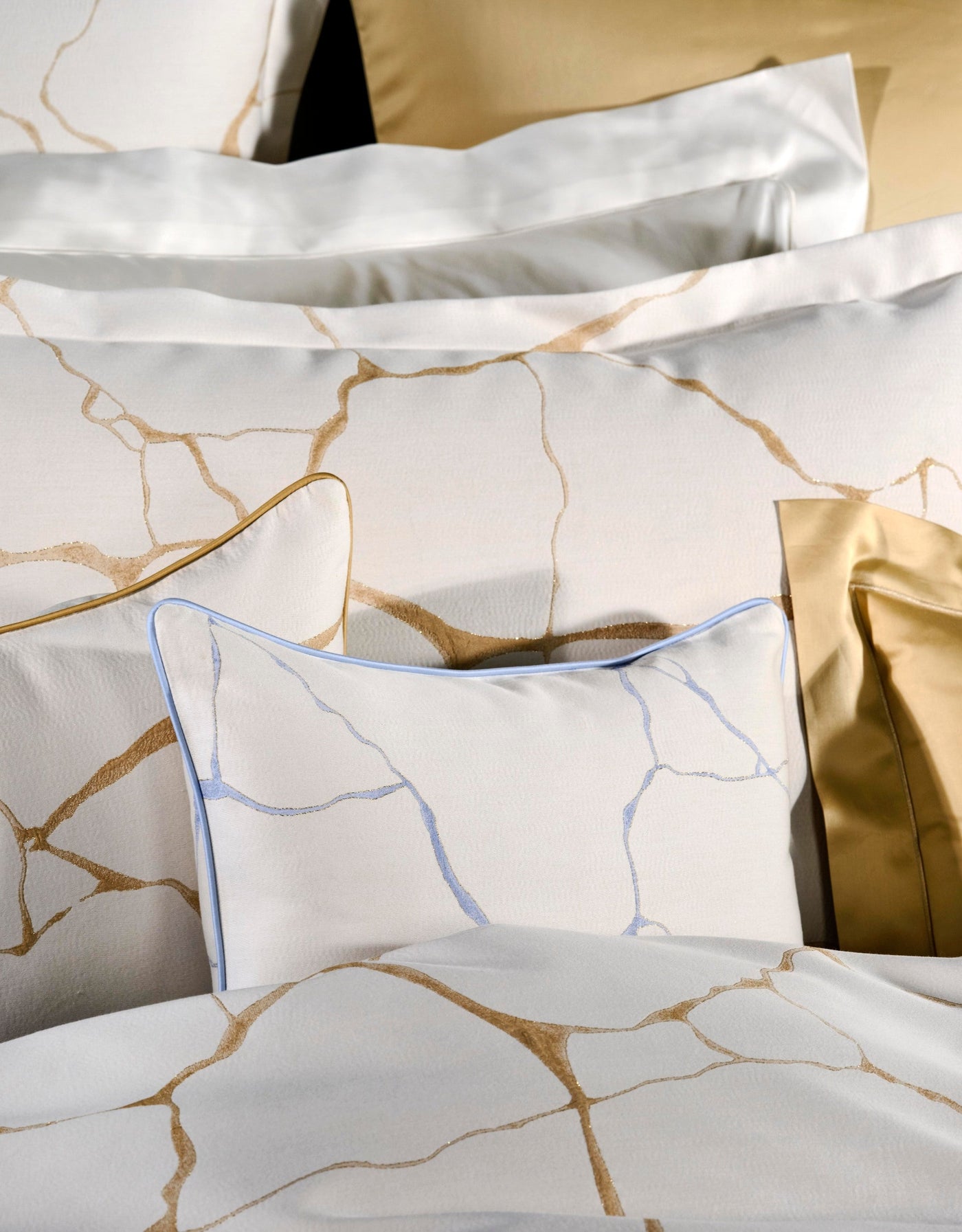 Close-up of white bedding with gold and blue marbled pattern, featuring Jessie Pillowcase by Celso de Lemos available at Linen Society.