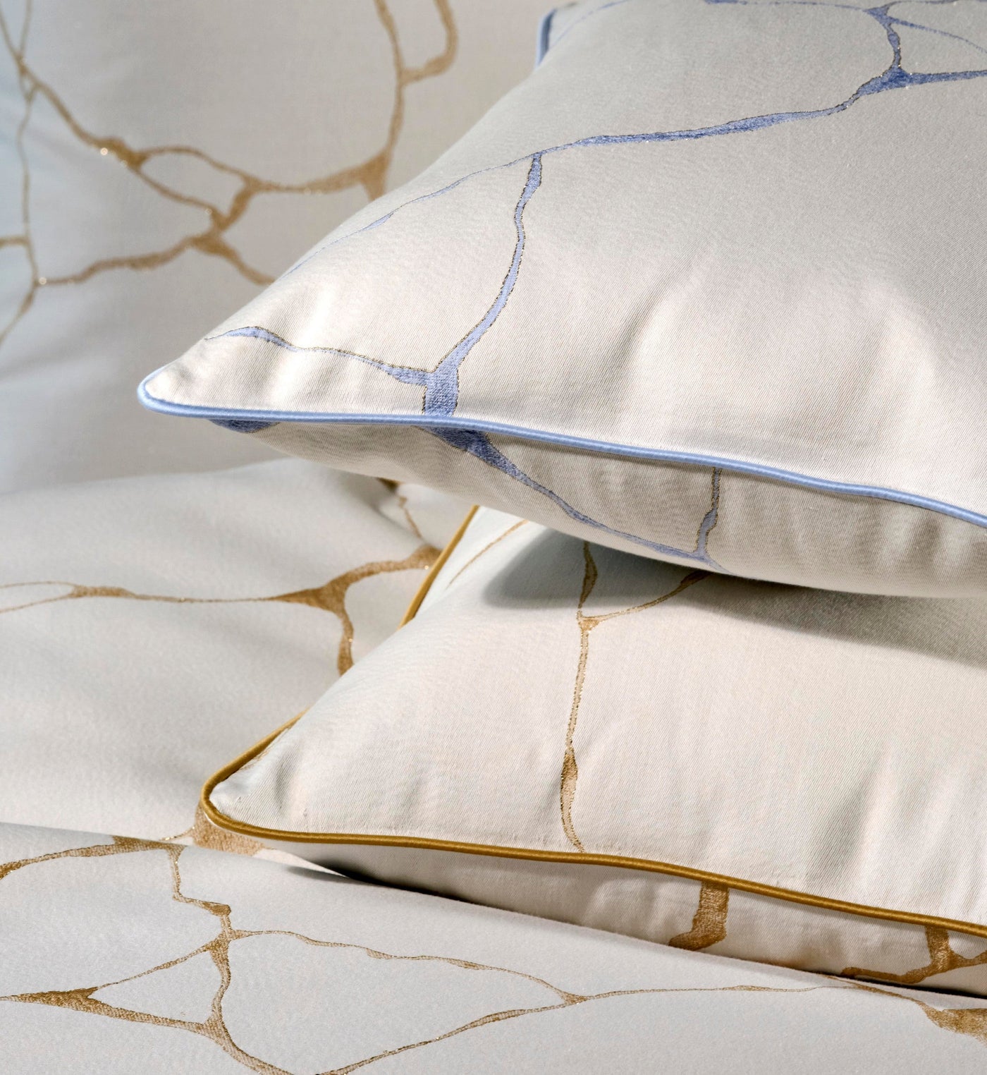 Closeup of white bedding with gold abstract pattern and piped edges, featuring Jessie Pillowcase by Celso de Lemos available at Linen Society.